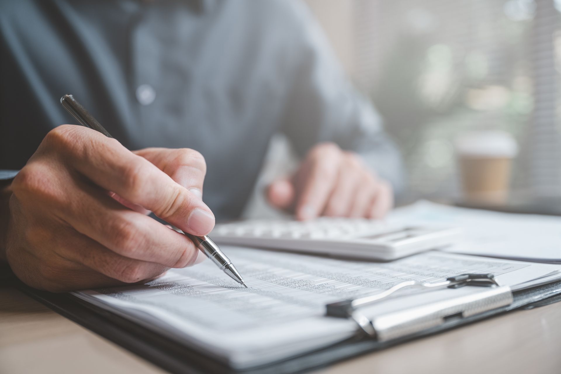 Person writing on a document with a pen, calculator in the background.