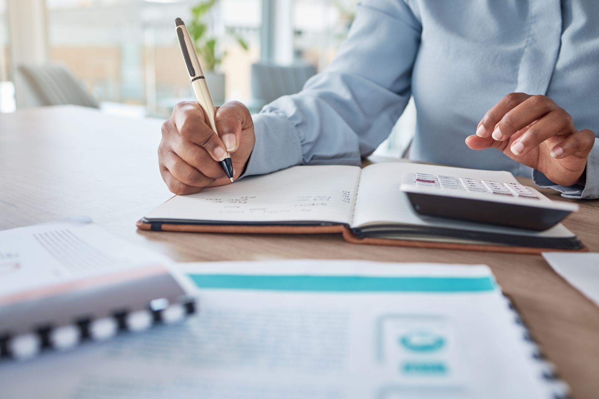 Person using a calculator and writing in a notebook at a desk