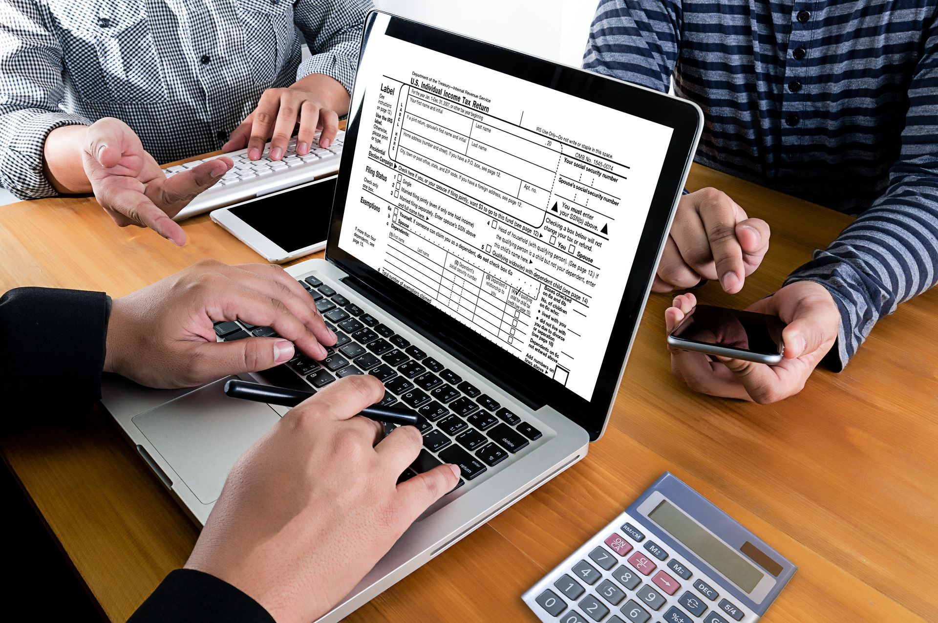 Three people review tax documents on a laptop