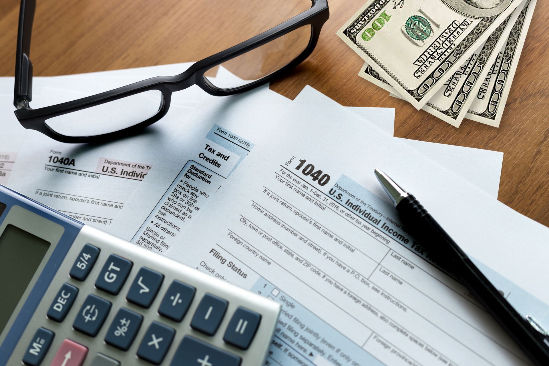 Tax forms, calculator, glasses, pen, and money on a wooden surface