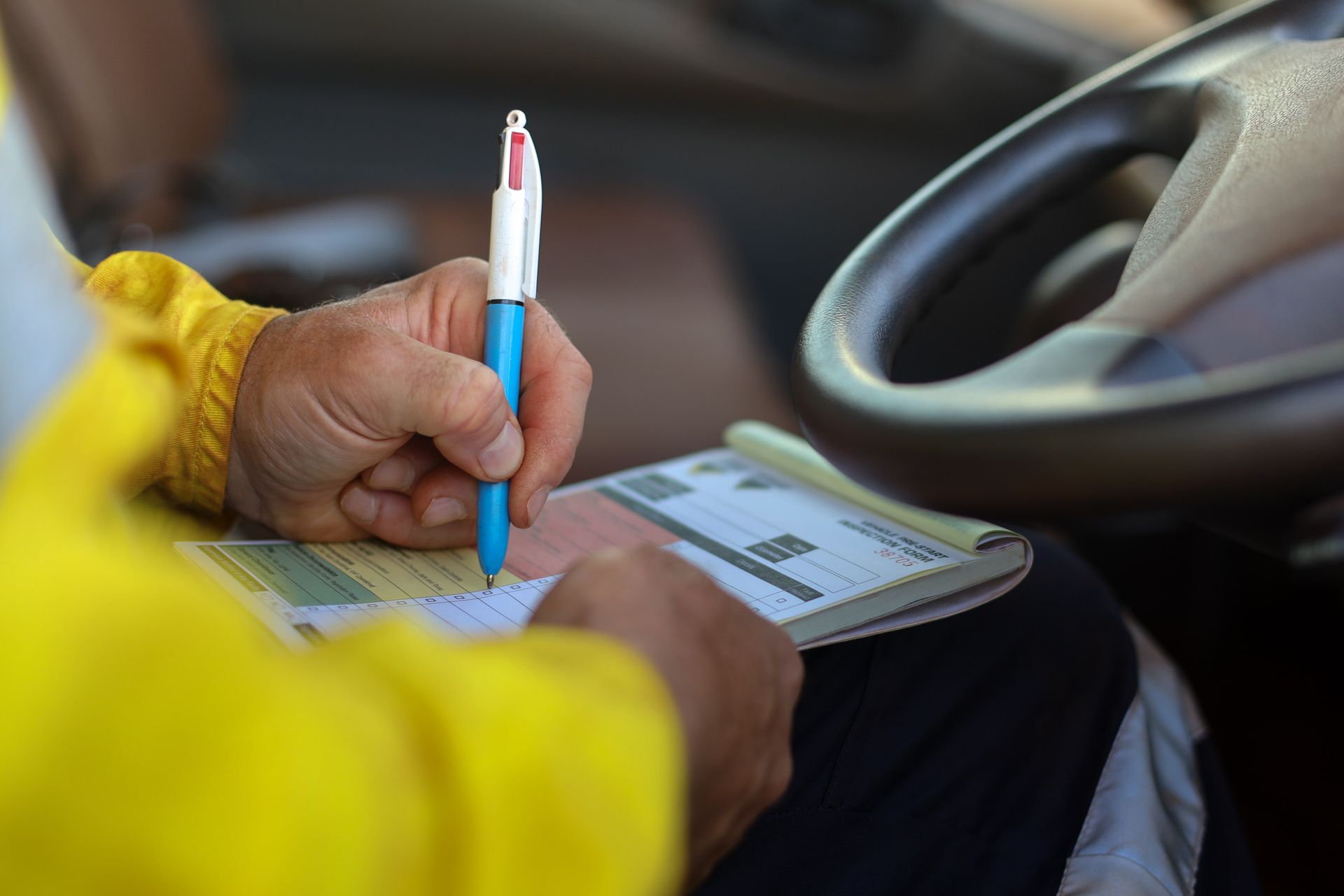 A Person Is Sitting in A Car Writing on A Piece of Paper with A Pen — BEB Automotive In Campbelltown, NSW
