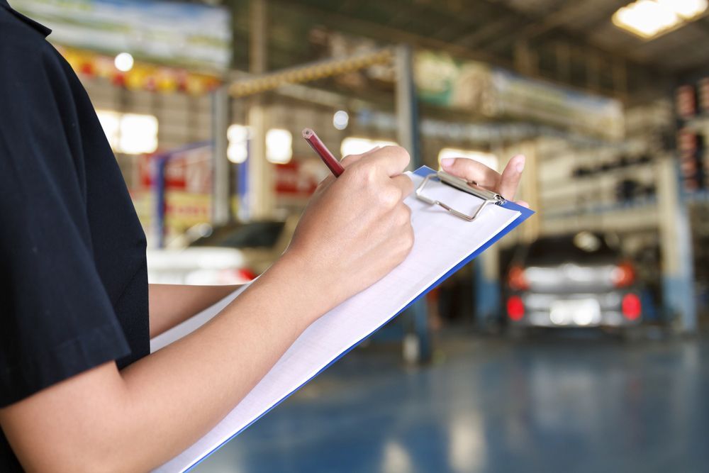 A Man Is Writing on A Clipboard in A Garage — BEB Automotive In Berkeley, NSW