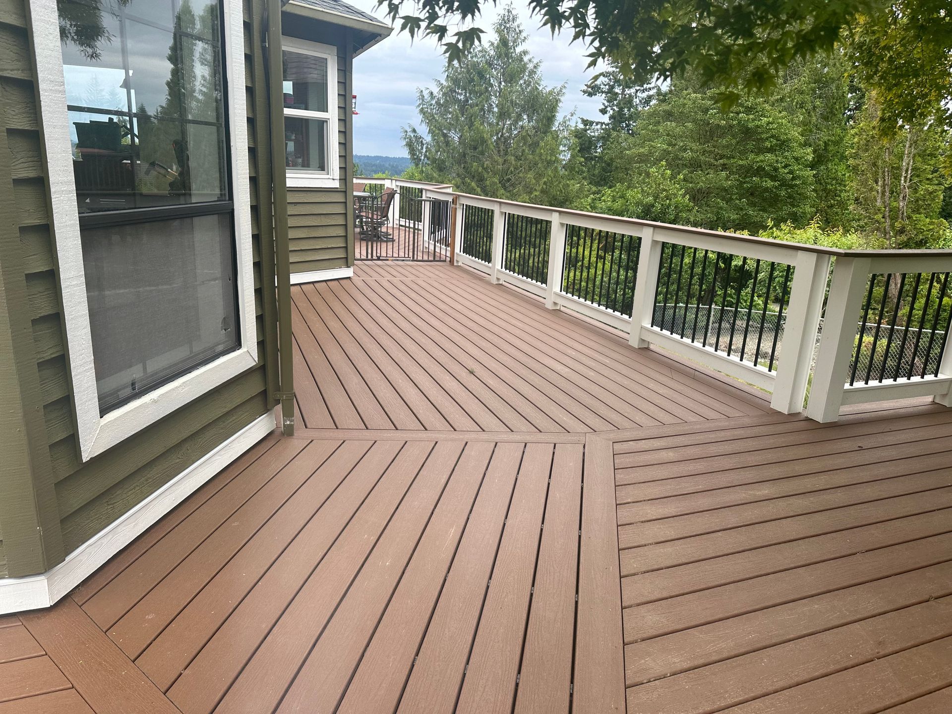 A large wooden deck with a white railing is sitting next to a house.