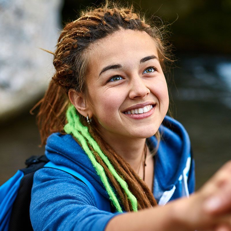 Woman with dreadlocks looks up smiling, wearing a blue hoodie.