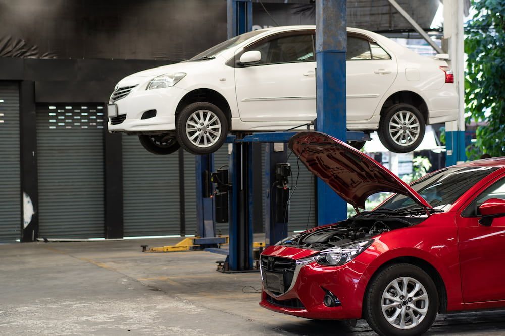 A Red Car Is Parked Next to A White Car on A Lift in A Garage — Palmerston Auto Clinic in Yarrawonga, NT
