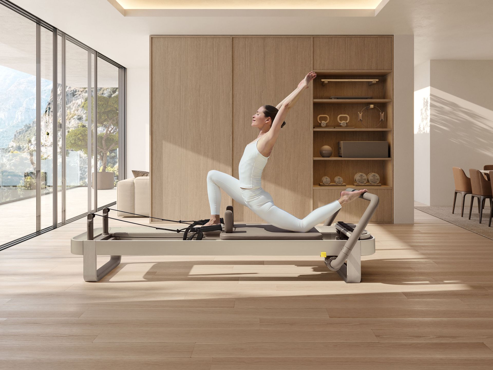 A person in light-colored activewear performs a single-leg pilates exercise on a reformer in a bright, minimalist studio.