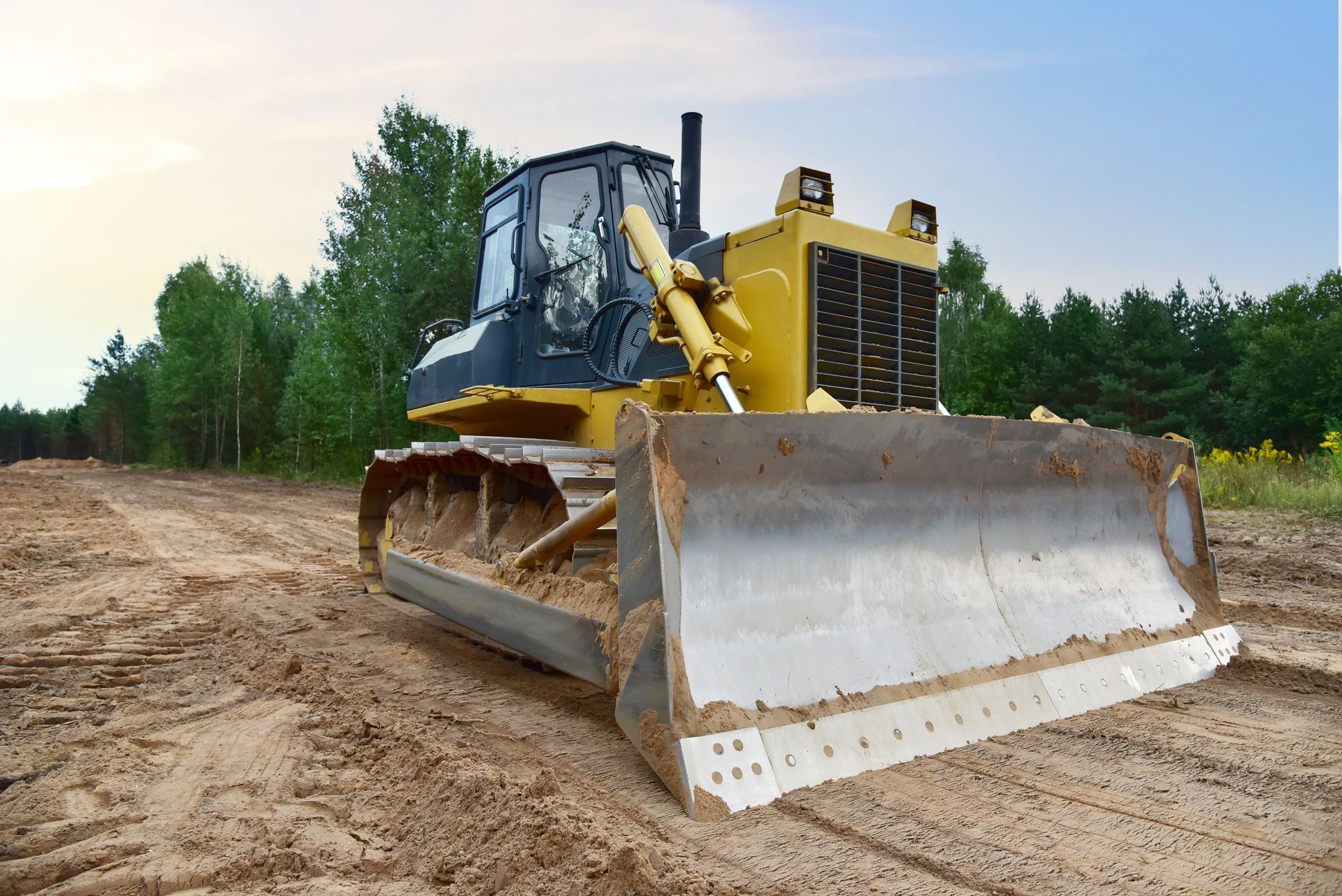 Yellow bulldozer on a dirt road at a construction site, front blade raised slightly.