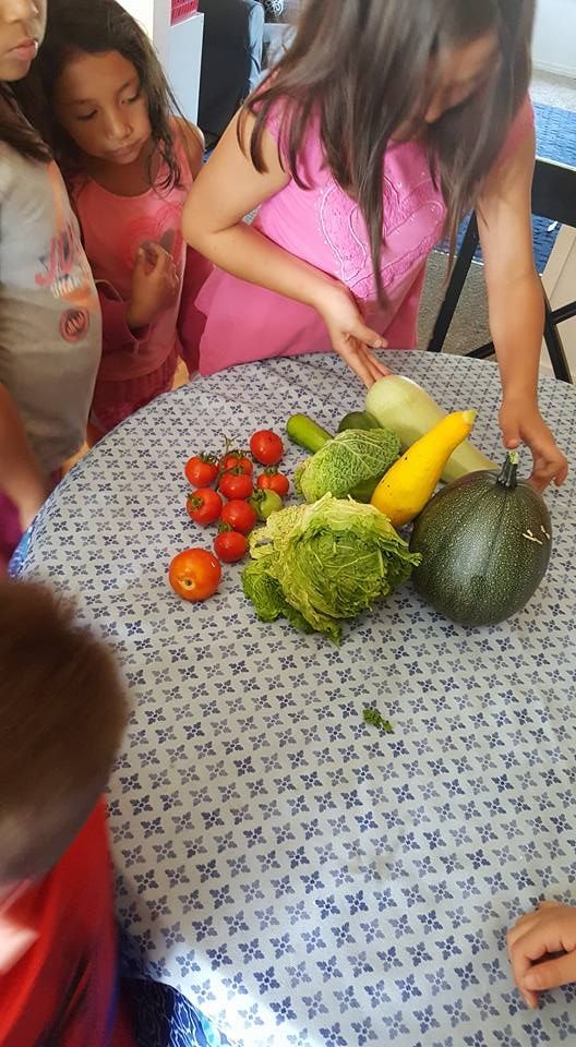 A group of children are standing around a table with vegetables on it.