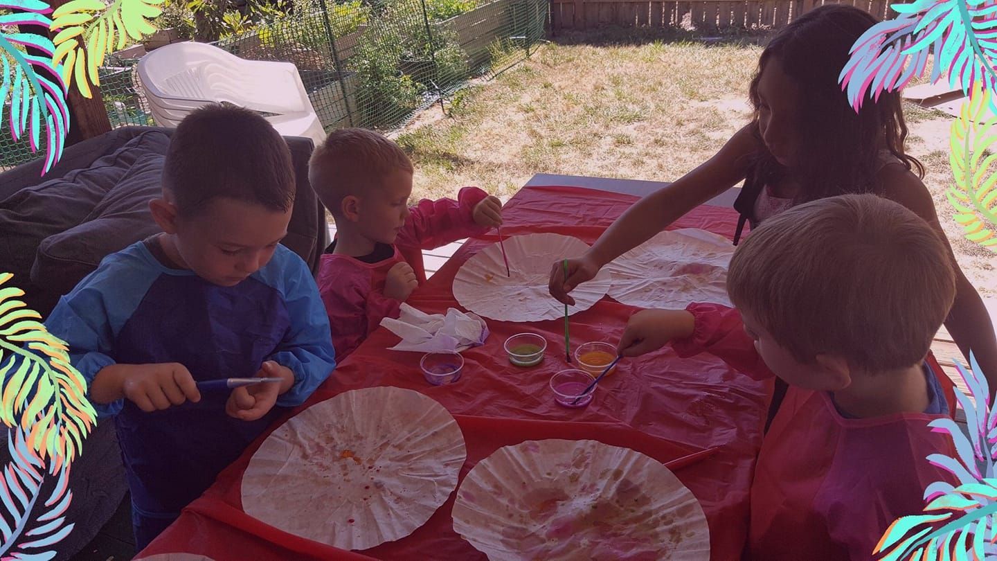 A group of children are sitting at a table making paper fans.
