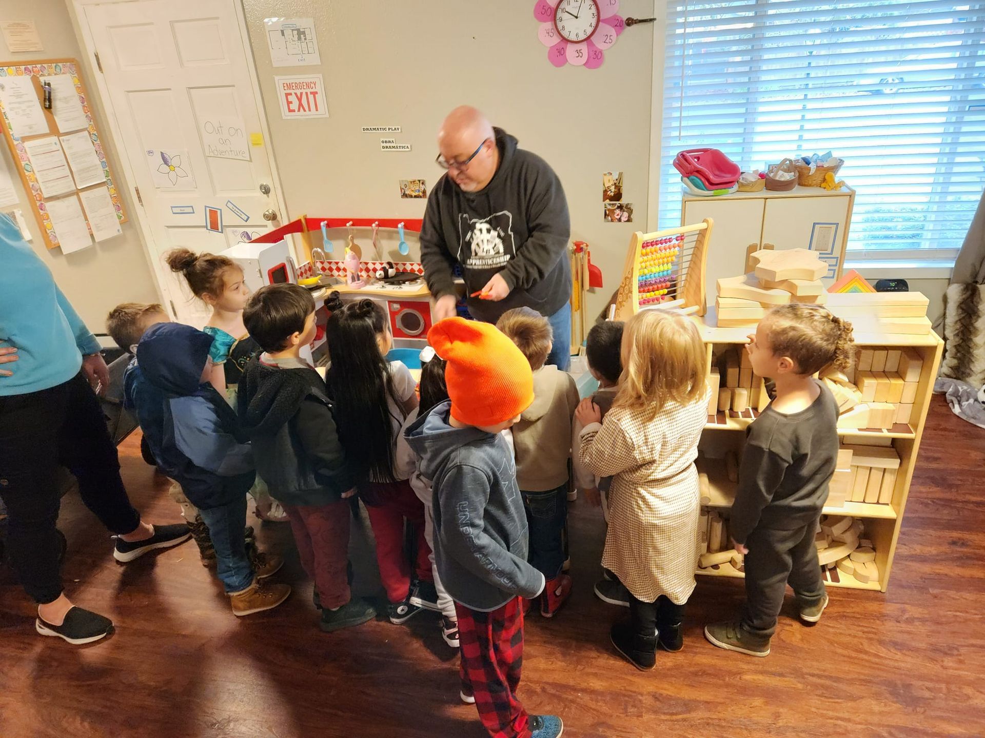 A group of children are standing around a man in a room.