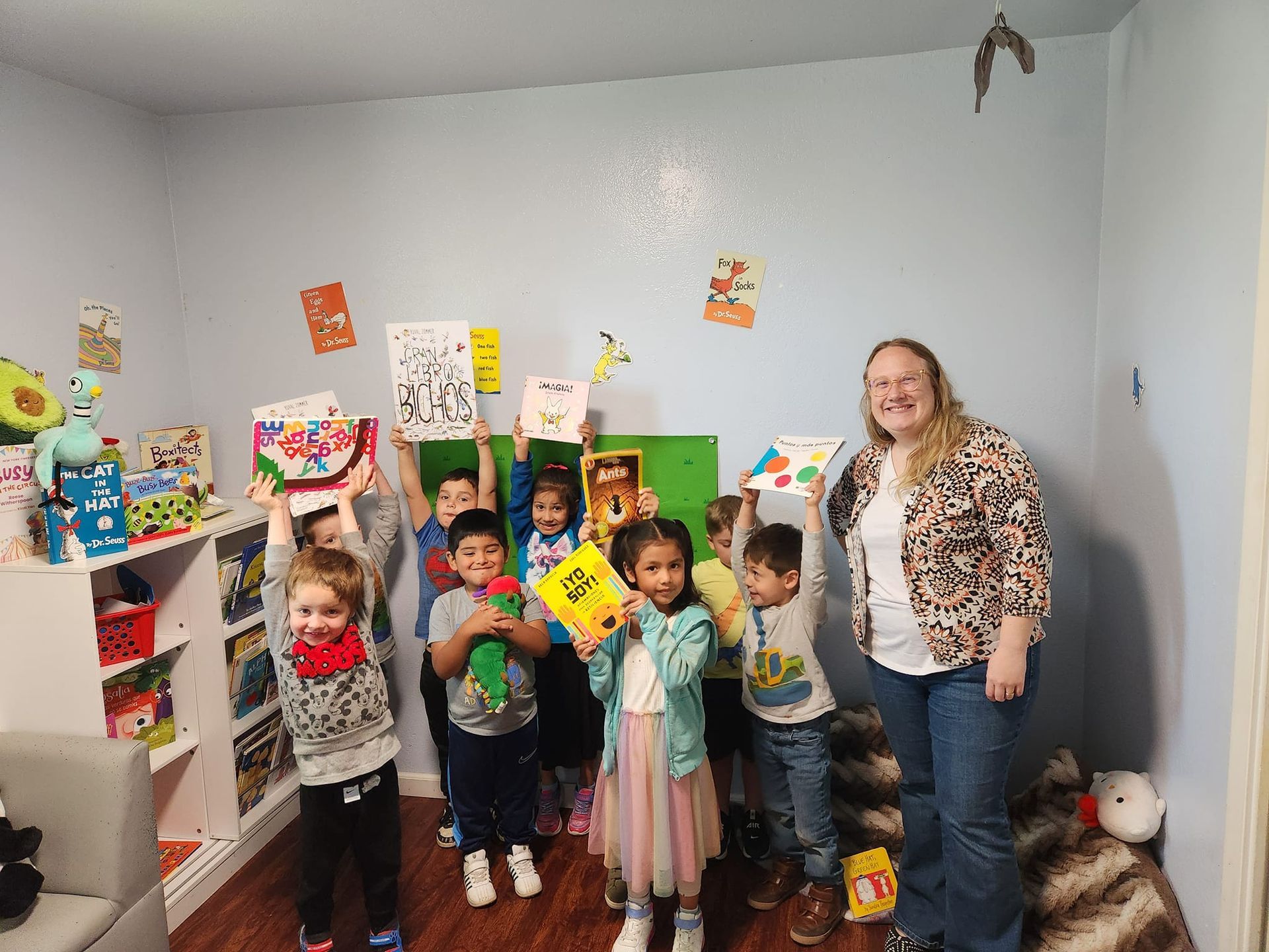 A group of children and a woman are standing in a room holding books.