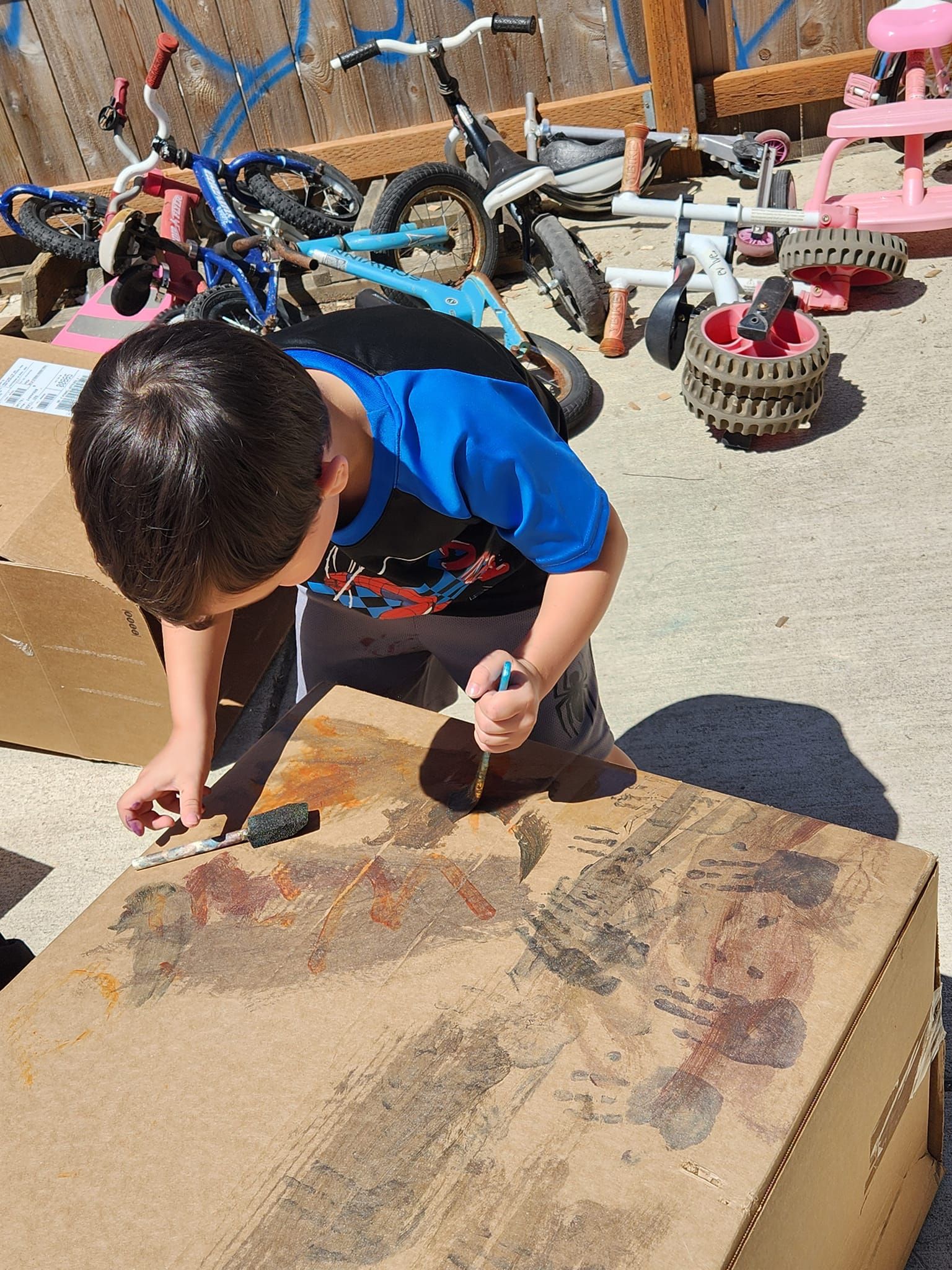 A young boy is painting a picture on a cardboard box.