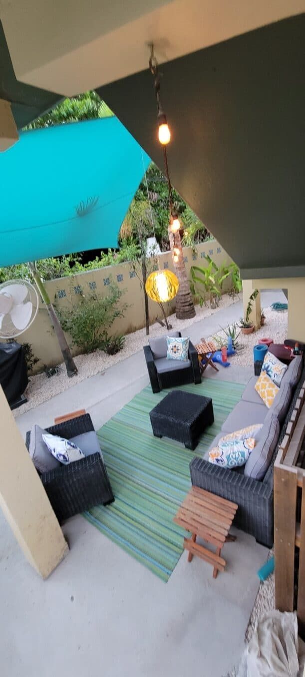 A patio with a couch , chairs , ottoman and umbrella.