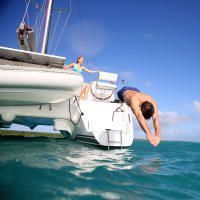 A man is diving off of a sailboat into the ocean.