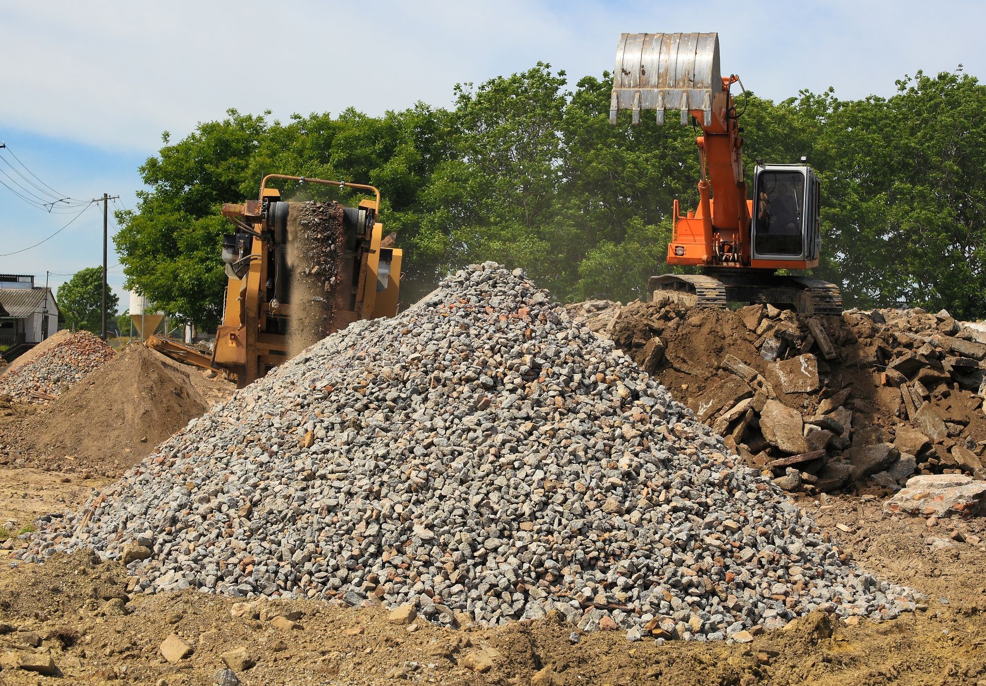 A stone crusher and crane working outdoors with large piles of aggregates around them.