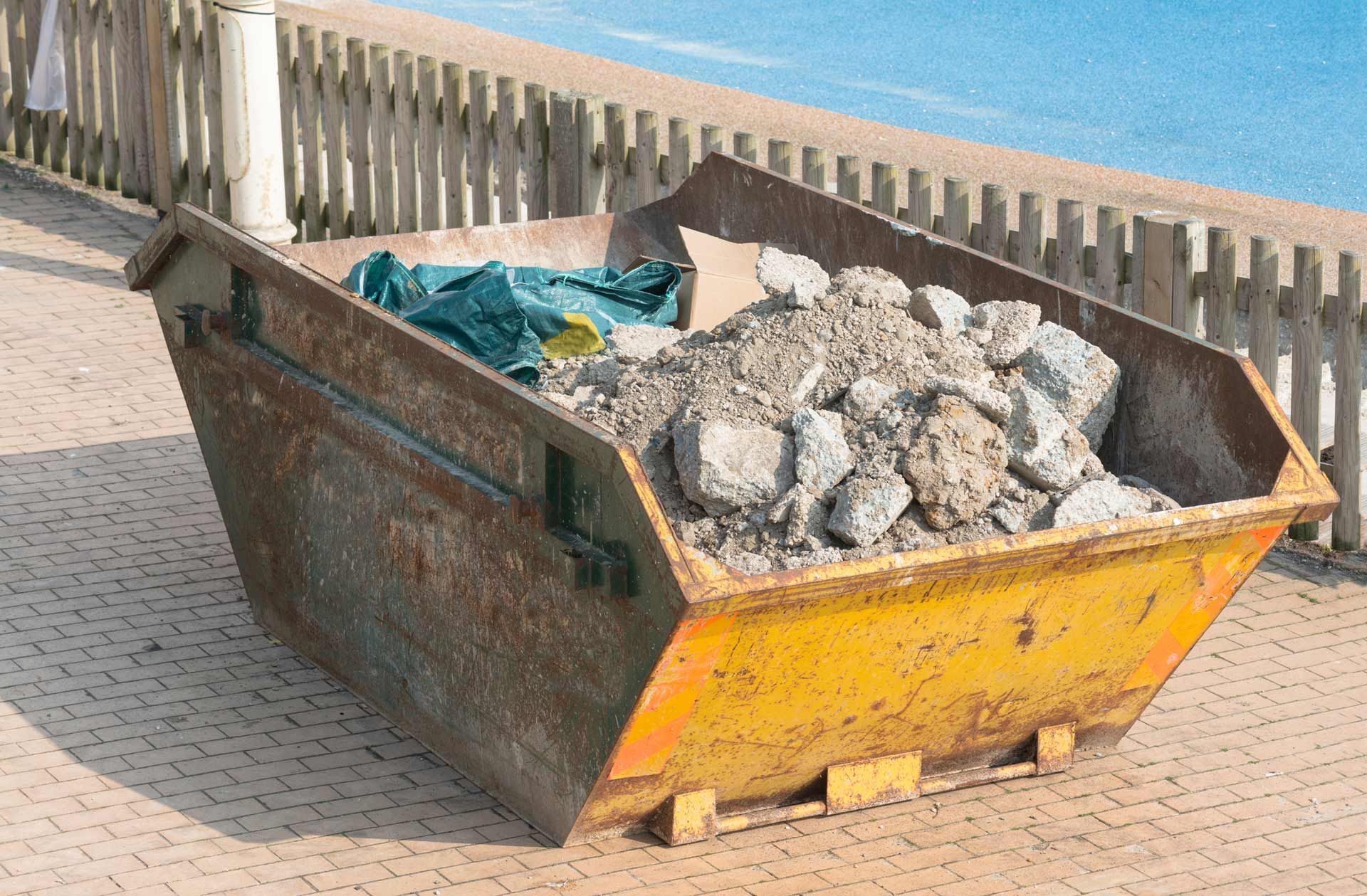 A dumpster filled with rocks is sitting next to a pool.