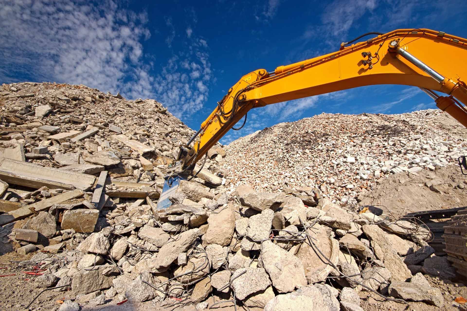 A yellow excavator is working on a pile of rocks.