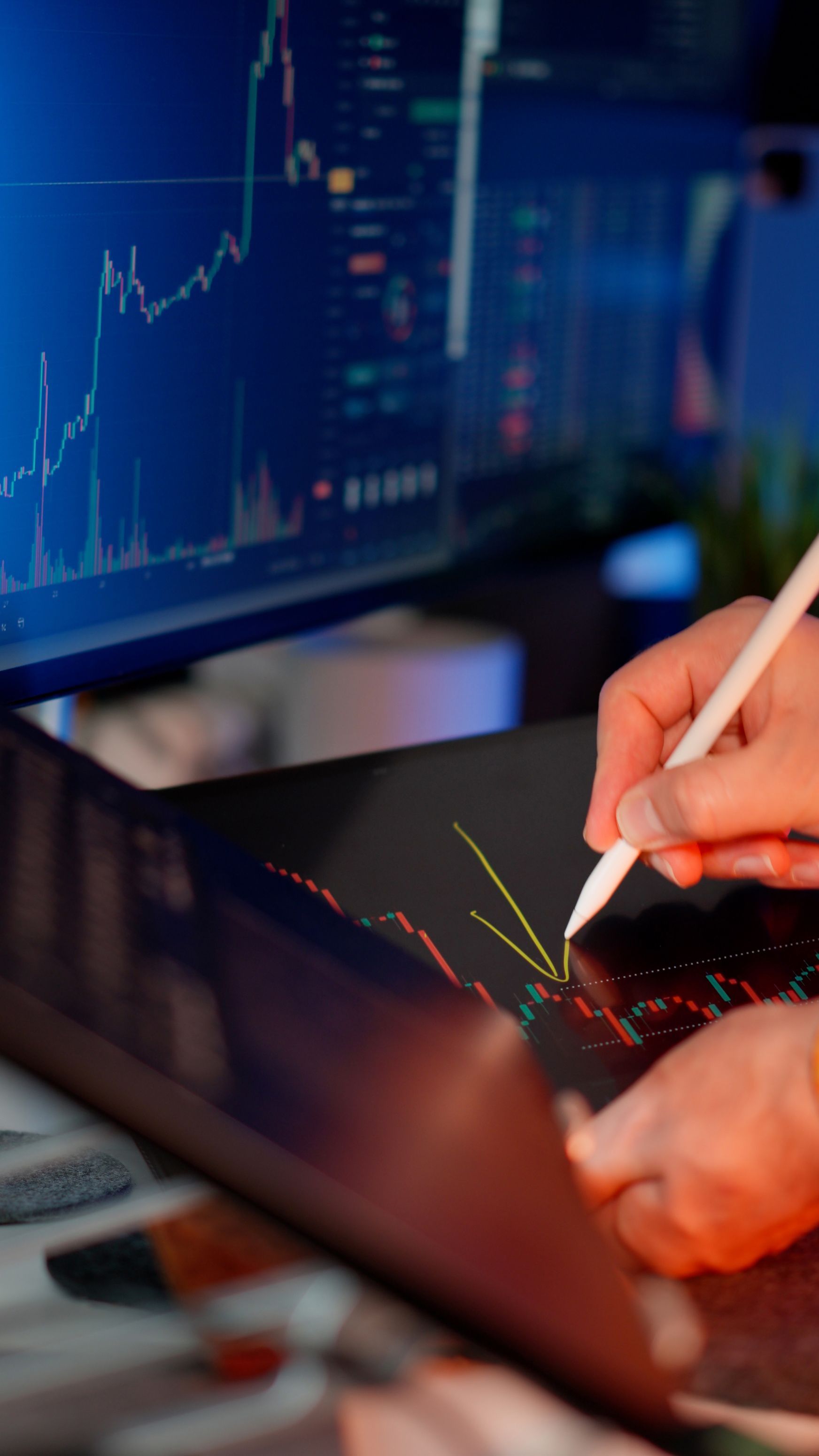 Hand writing on a laptop beside a glowing stock market chart screen showing data system implementation by Wilsona Marketing