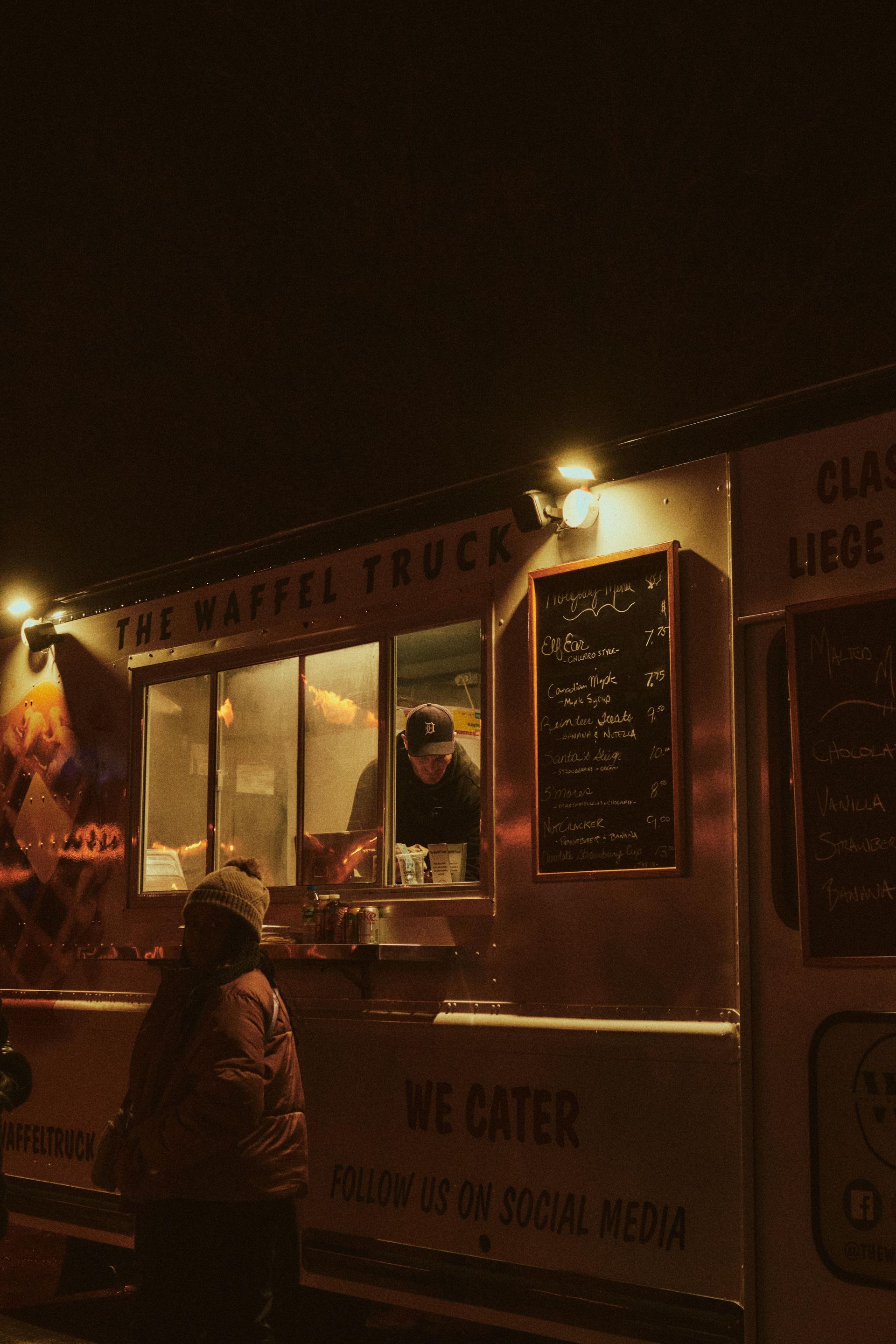 Food truck at night with customer ordering under lights and menu board. Truck growing with reputation management services