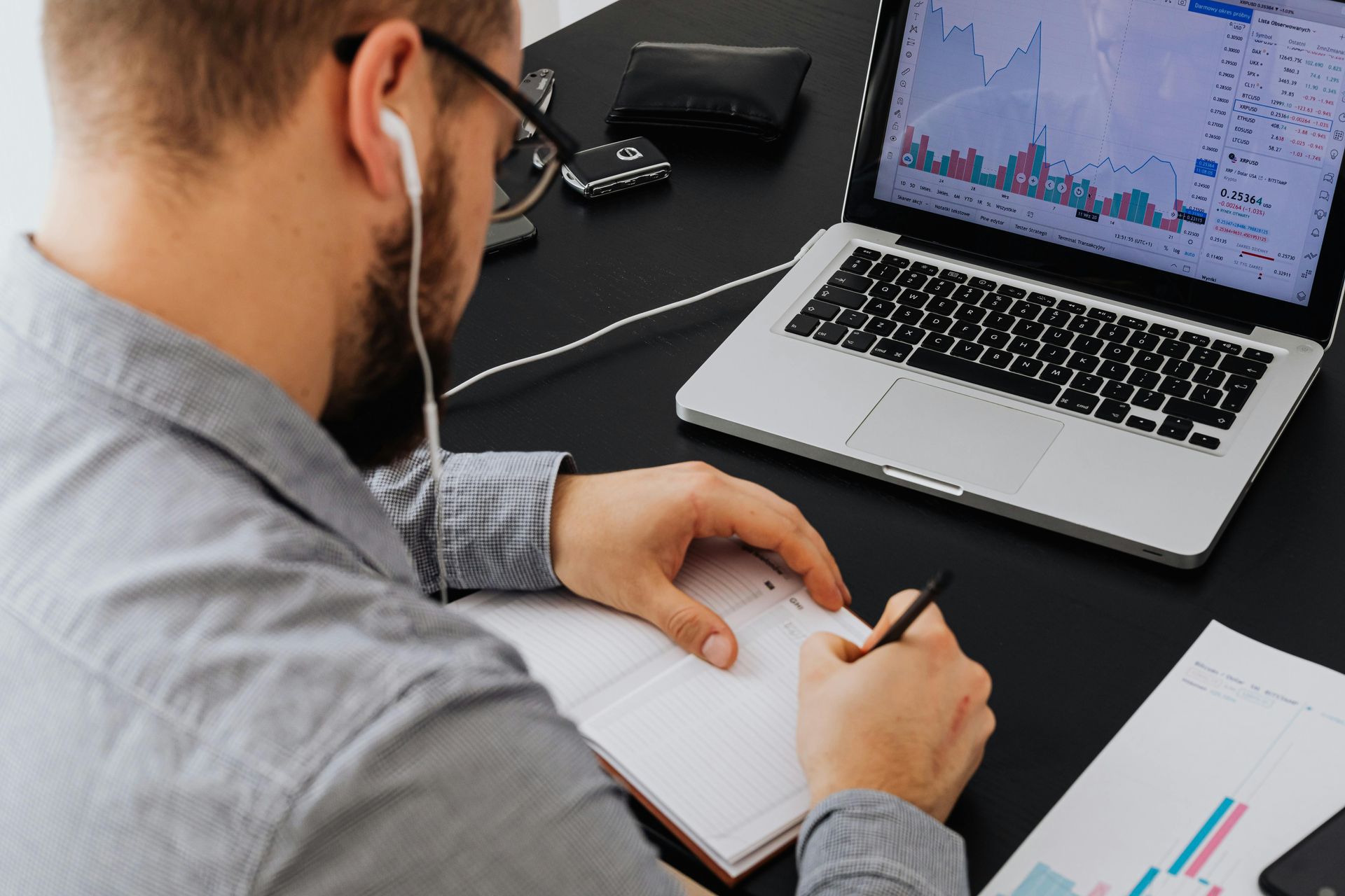 Man reviewing charts on a laptop while writing notes in a notebook at a desk at Wilsona Marketing