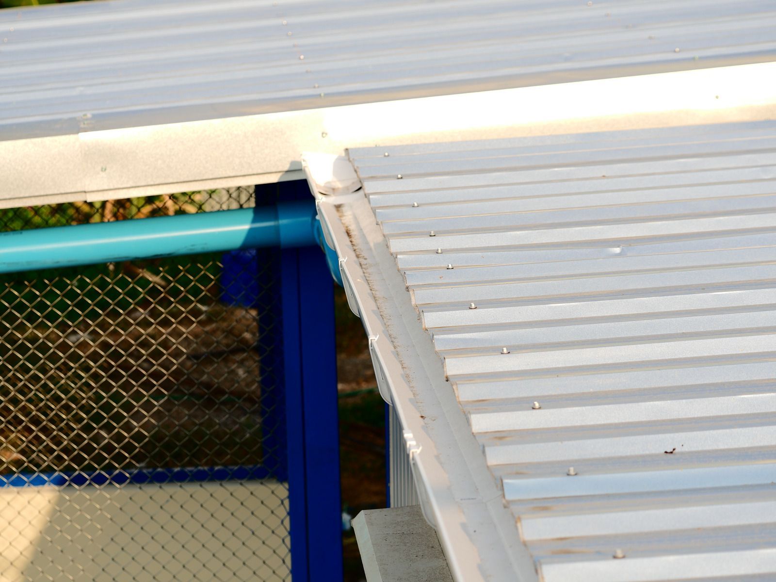 Corrugated metal roof detail; white with a blue pipe and support.