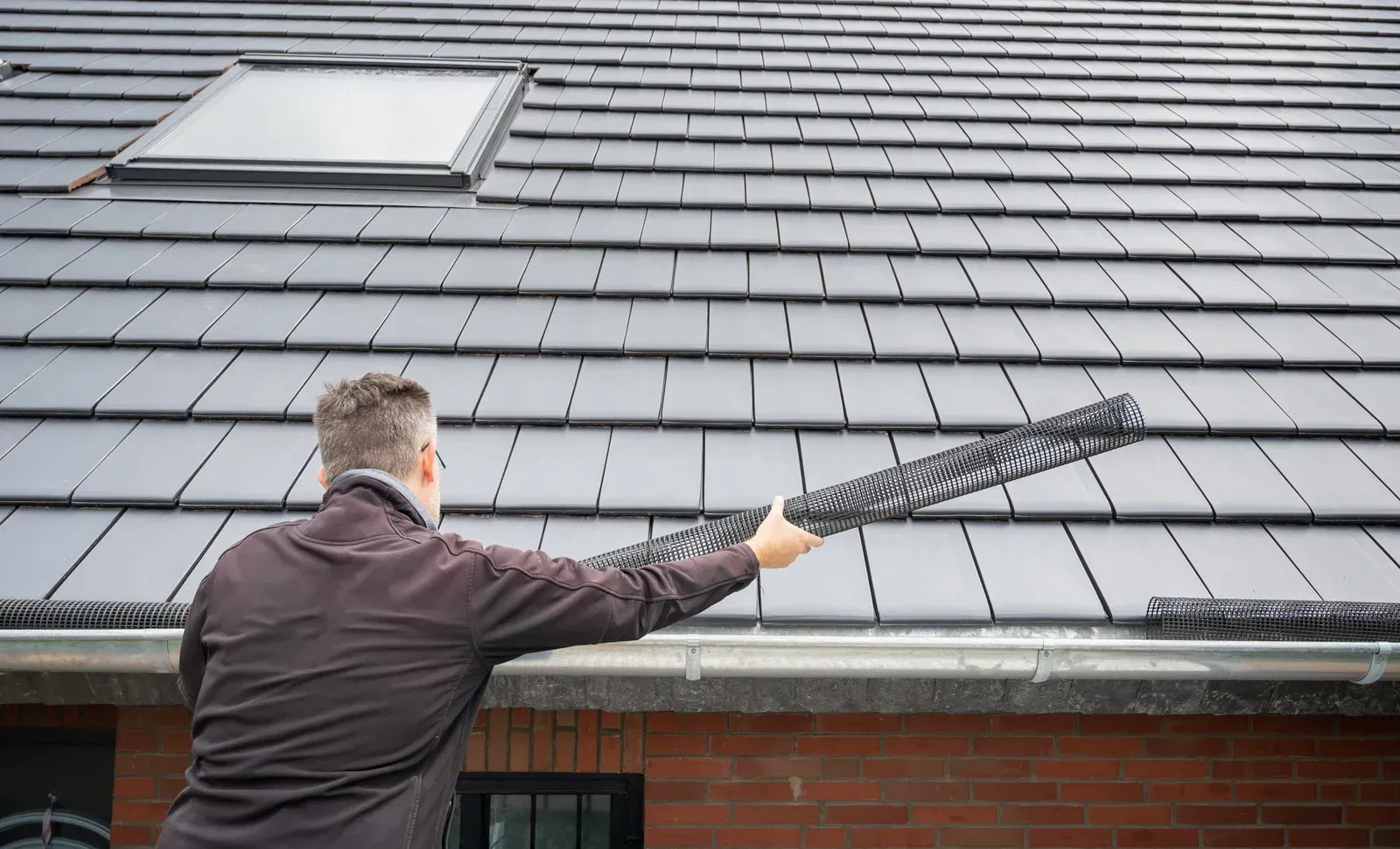 A man is cleaning the gutters of a roof with a broom.