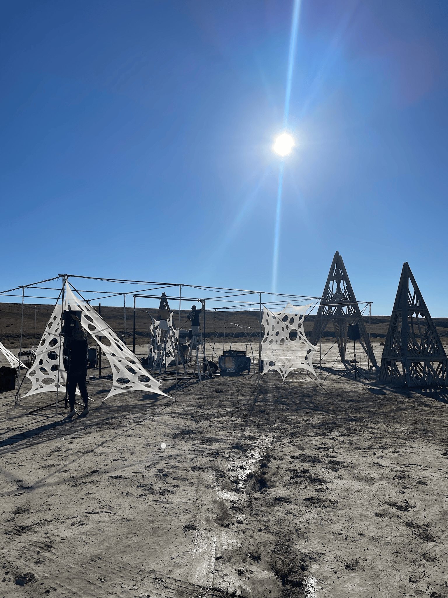 Person standing near abstract art installations under a bright sun.