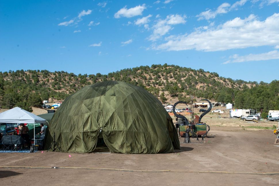 Green dome tent at a campsite with vehicles and mountains under a blue sky