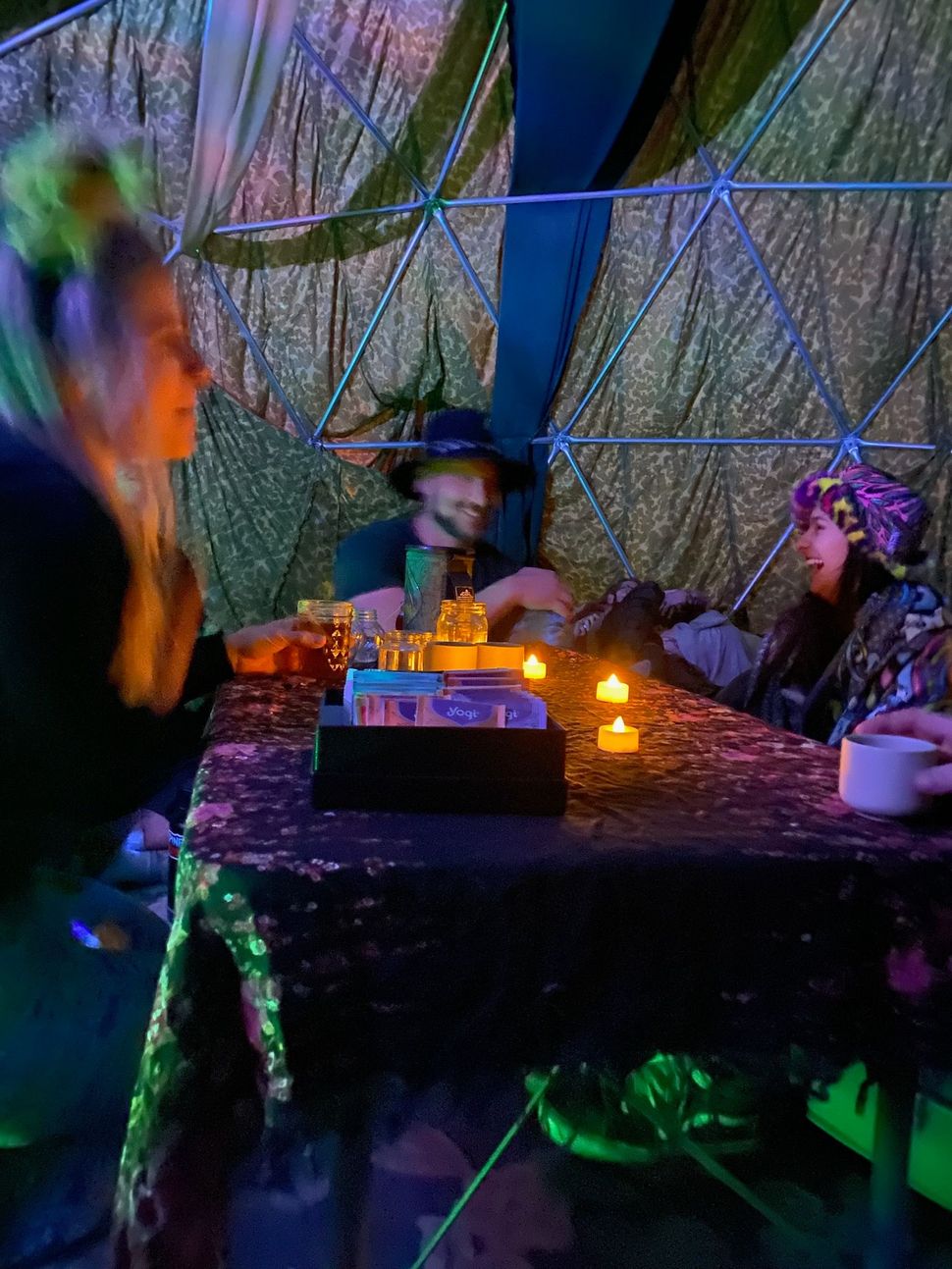People seated at a dimly lit table in a colorful, net-covered indoor scene with glowing candles
