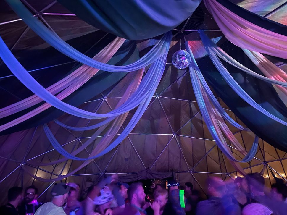 Crowd dancing under draped purple and blue fabric lights in a tent-like venue