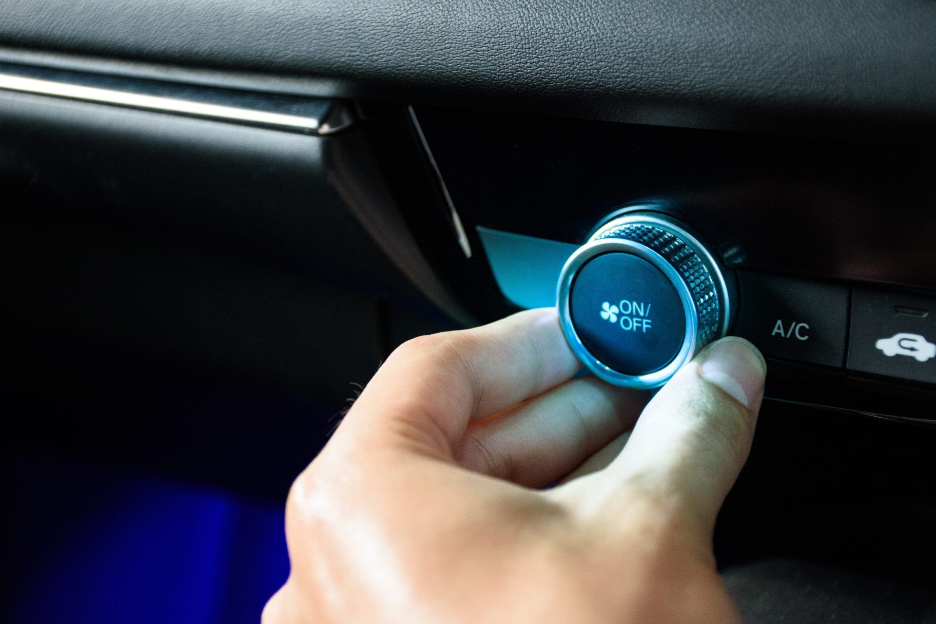 Hand turning a blue-lit car climate control dial on the dashboard