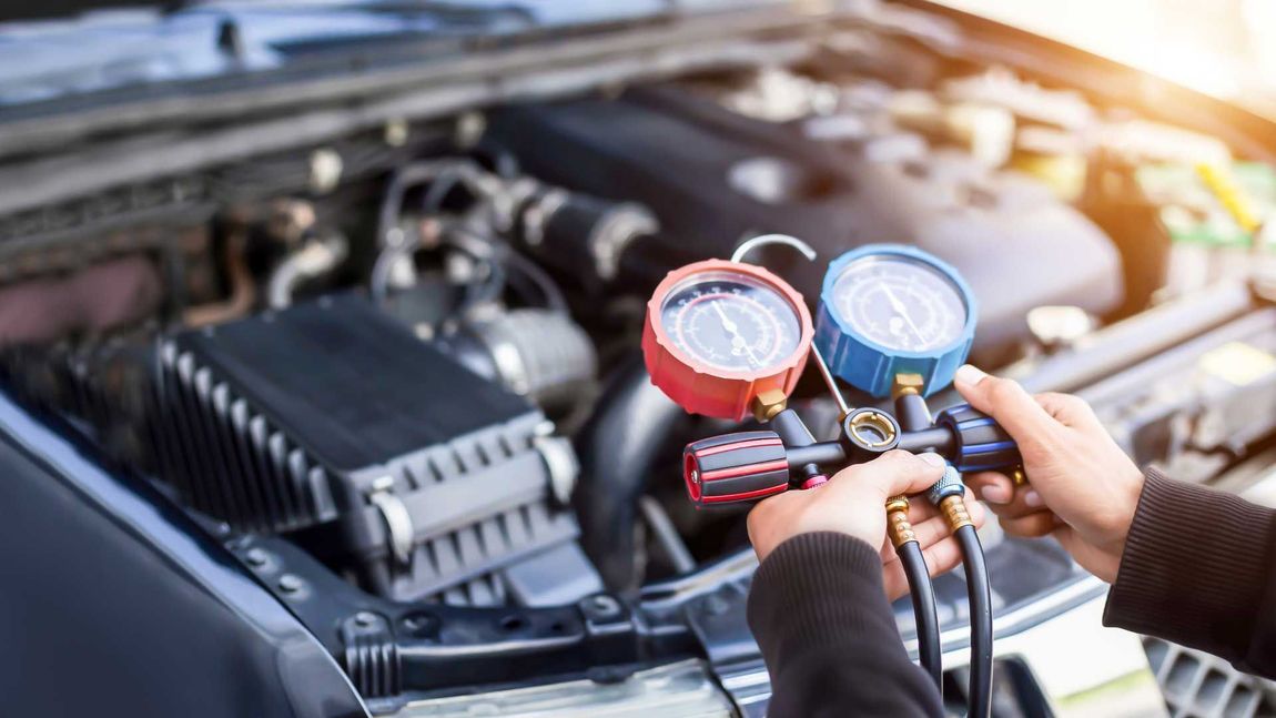 Hands holding red and blue gauges near a car engine during air conditioning service