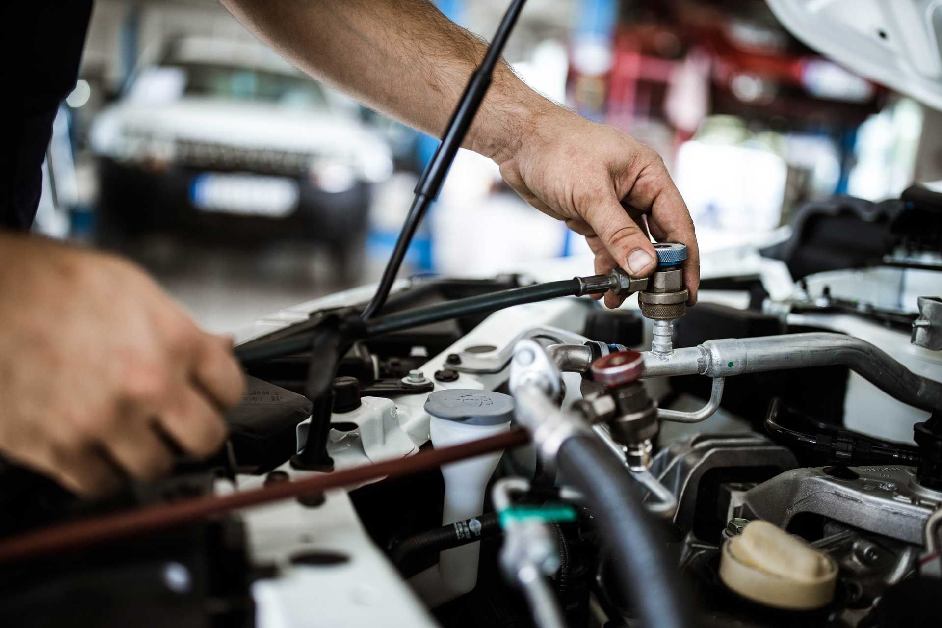 Mechanic’s hands working under an open car hood with tools in a repair shop