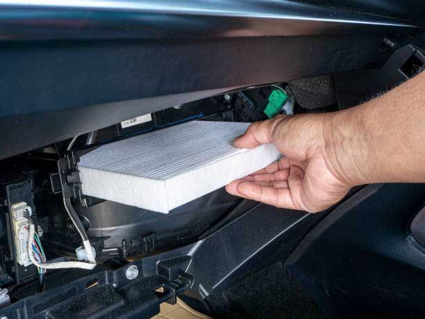 Hand replacing a white cabin air filter in a car dashboard compartment