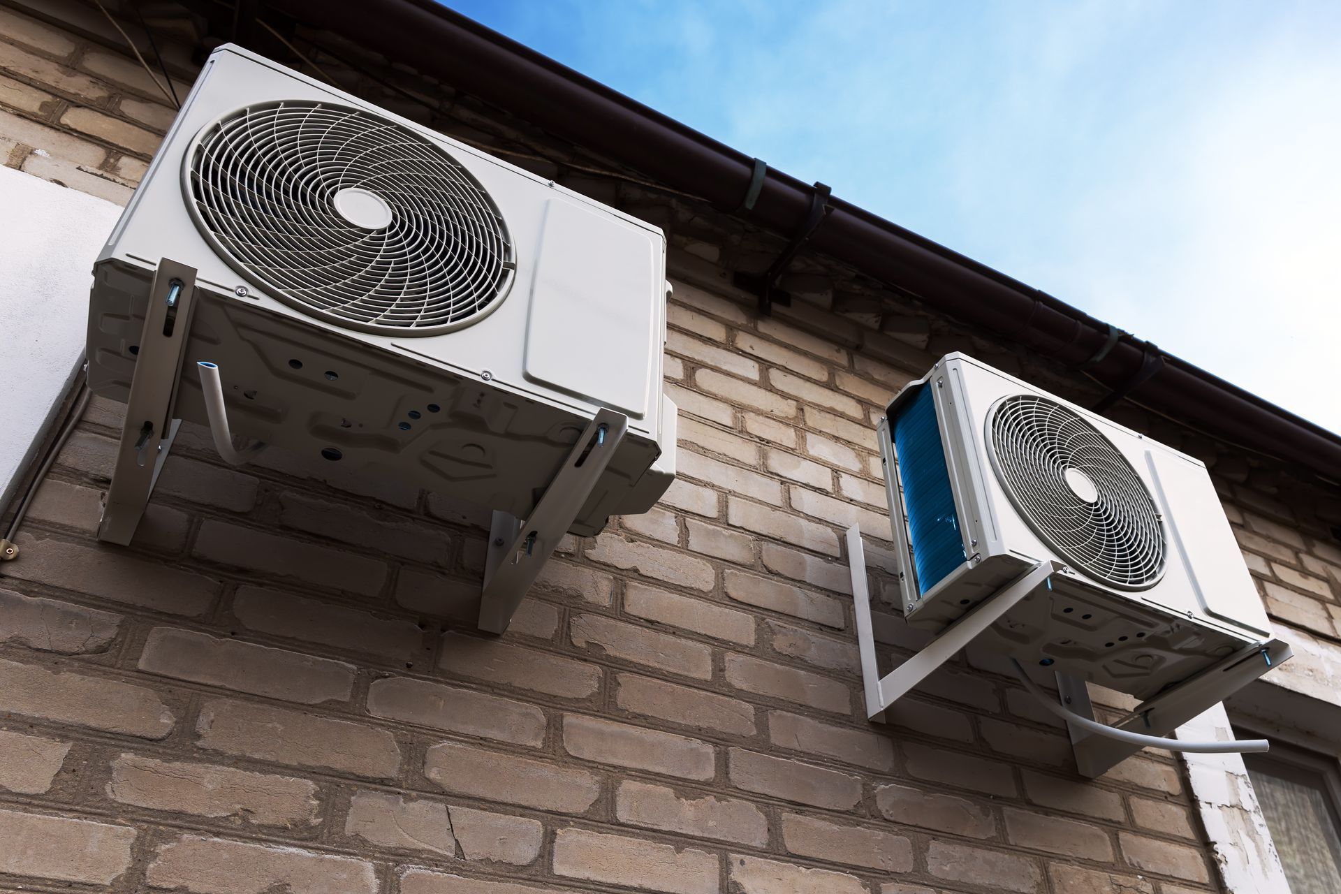 Two outdoor air conditioner units mounted on a brick building wall under a blue sky Two outdoor air conditioner units mounted on a brick building wall under a blue sky
