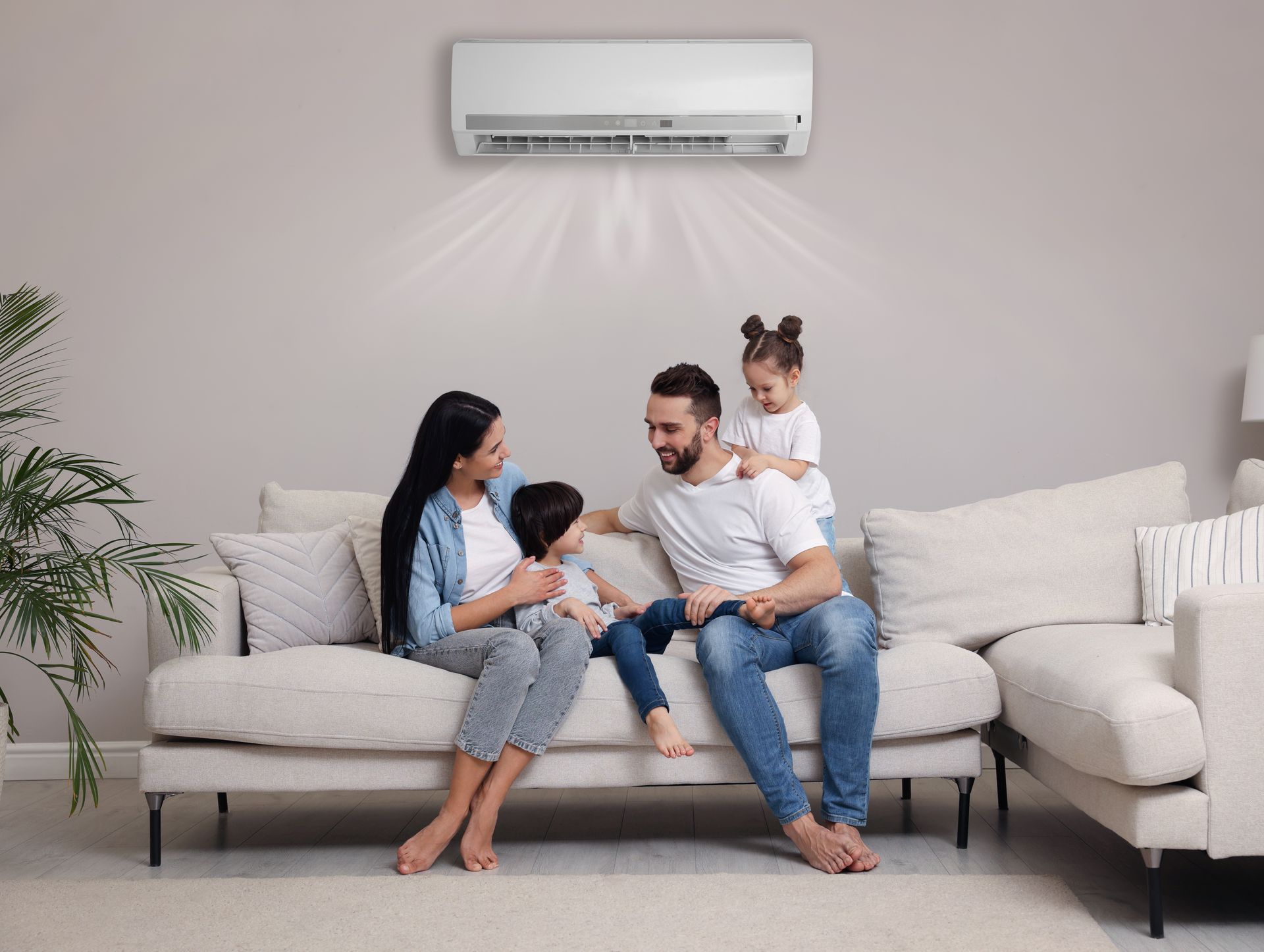Family sitting on a gray sofa in a bright living room under a wall-mounted air conditioner Family sitting on a gray sofa in a bright living room under a wall-mounted air conditioner