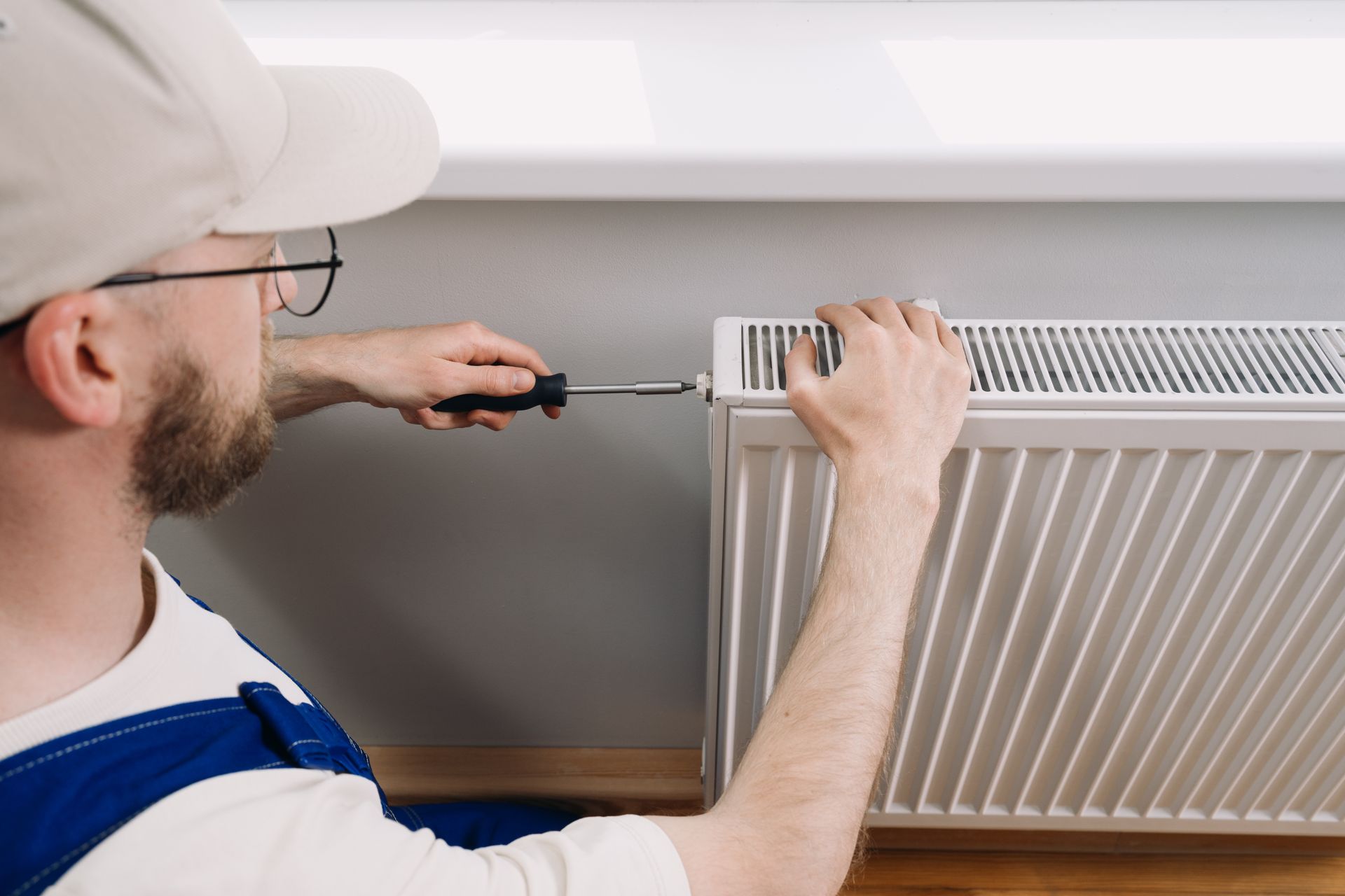 Person installing a wall radiator with a screwdriver in a home interior Person installing a wall radiator with a screwdriver in a home interior