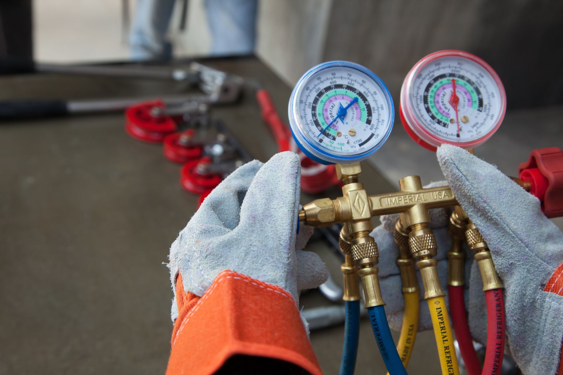 Gloved hands adjusting dual HVAC manifold gauges with red and blue hoses attached to metal valves. Gloved hands adjusting dual HVAC manifold gauges with red and blue hoses attached to metal valves.