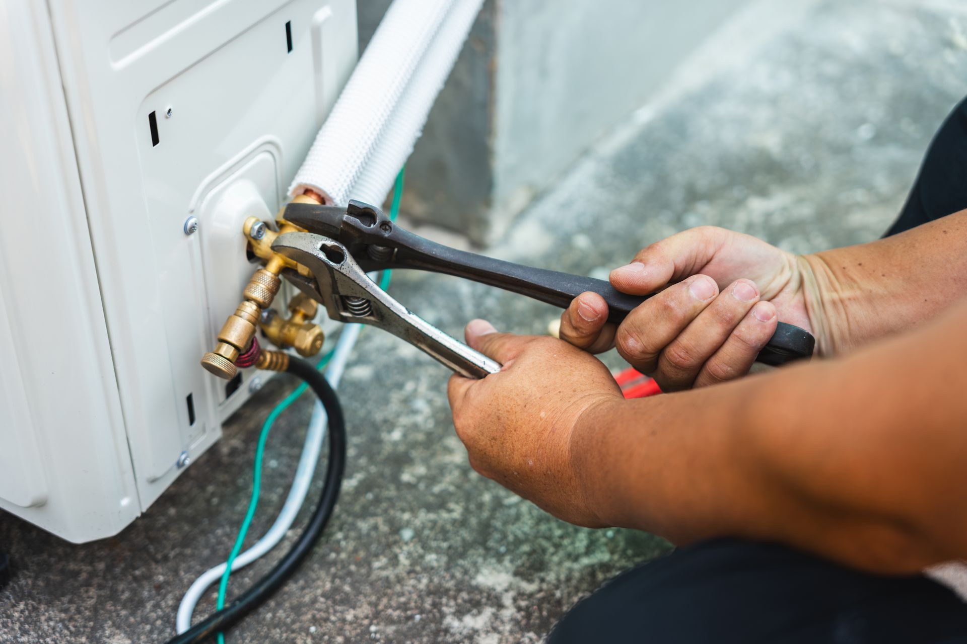 Hands using pliers to repair a water valve under an appliance, with hoses attached. Hands using pliers to repair a water valve under an appliance, with hoses attached.