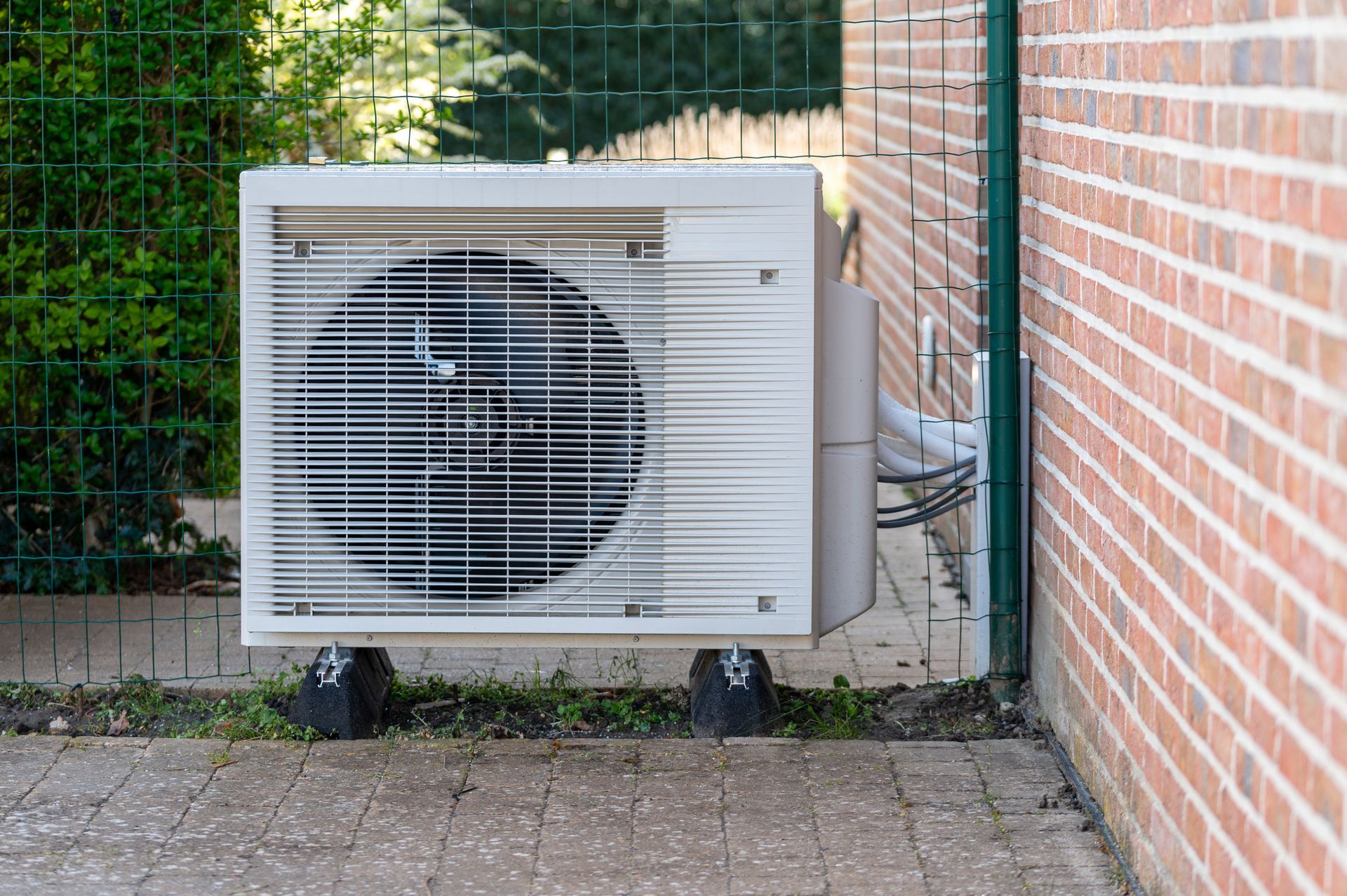 Outdoor air conditioner unit beside a brick wall and fence on a paved patio Outdoor air conditioner unit beside a brick wall and fence on a paved patio