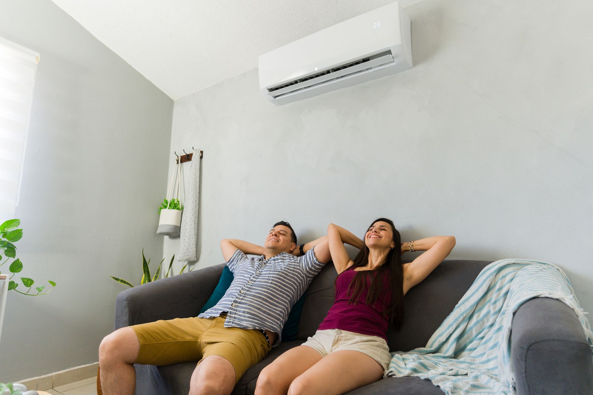 Two people relaxing on a sofa in a bright living room beneath a wall-mounted air conditioner Two people relaxing on a sofa in a bright living room beneath a wall-mounted air conditioner