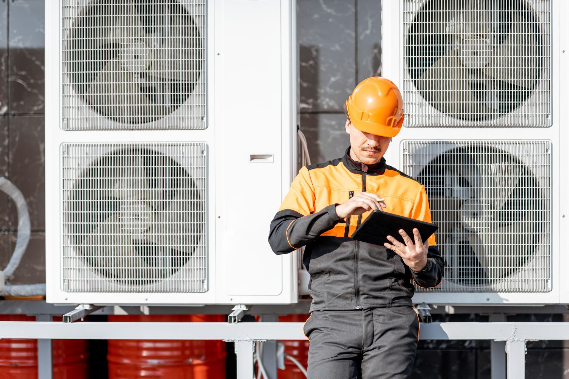 Worker in orange hard hat inspecting a tablet in front of large industrial fans. Worker in orange hard hat inspecting a tablet in front of large industrial fans.