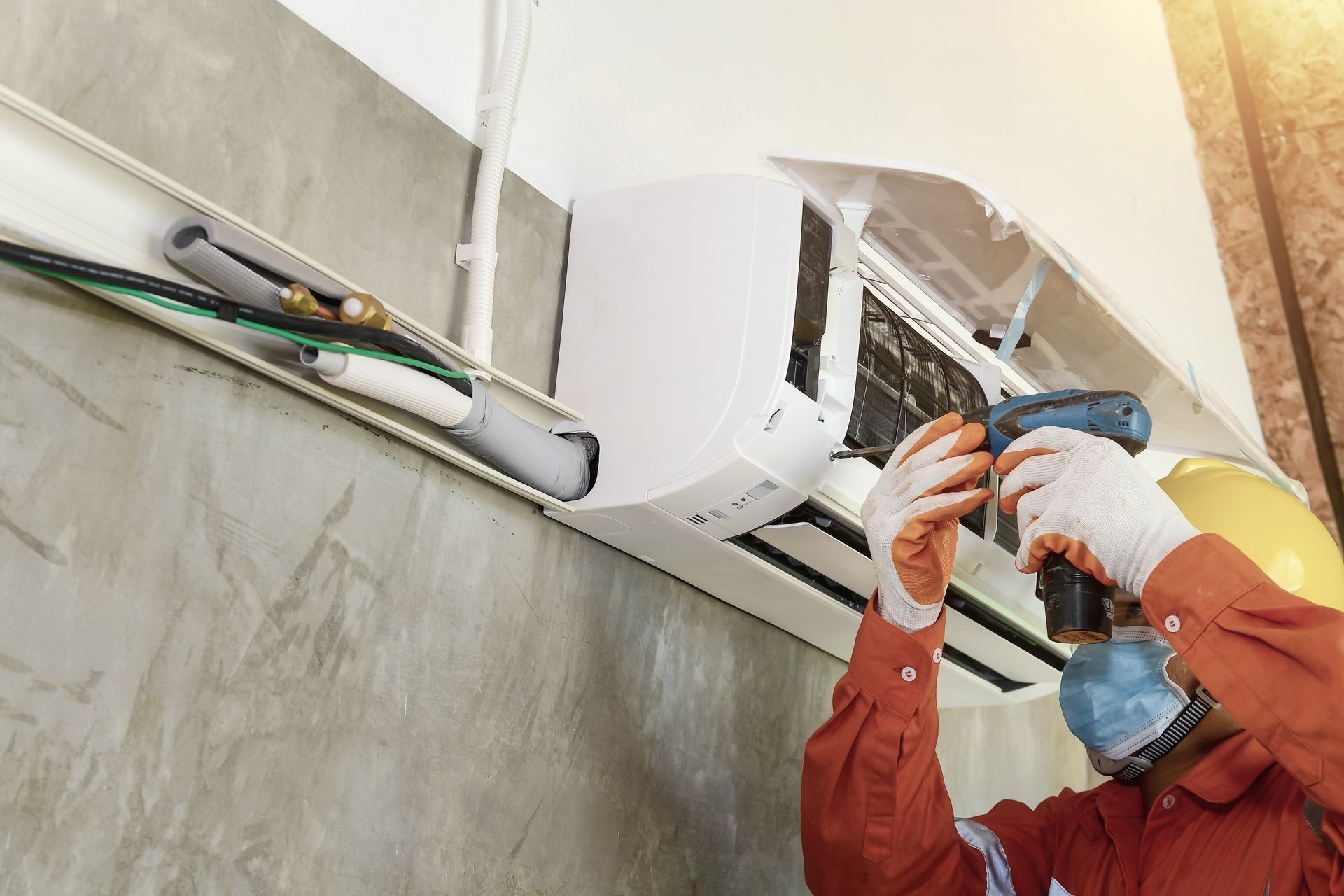 Technician installing or repairing a wall-mounted air conditioner with tools and safety mask Technician installing or repairing a wall-mounted air conditioner with tools and safety mask