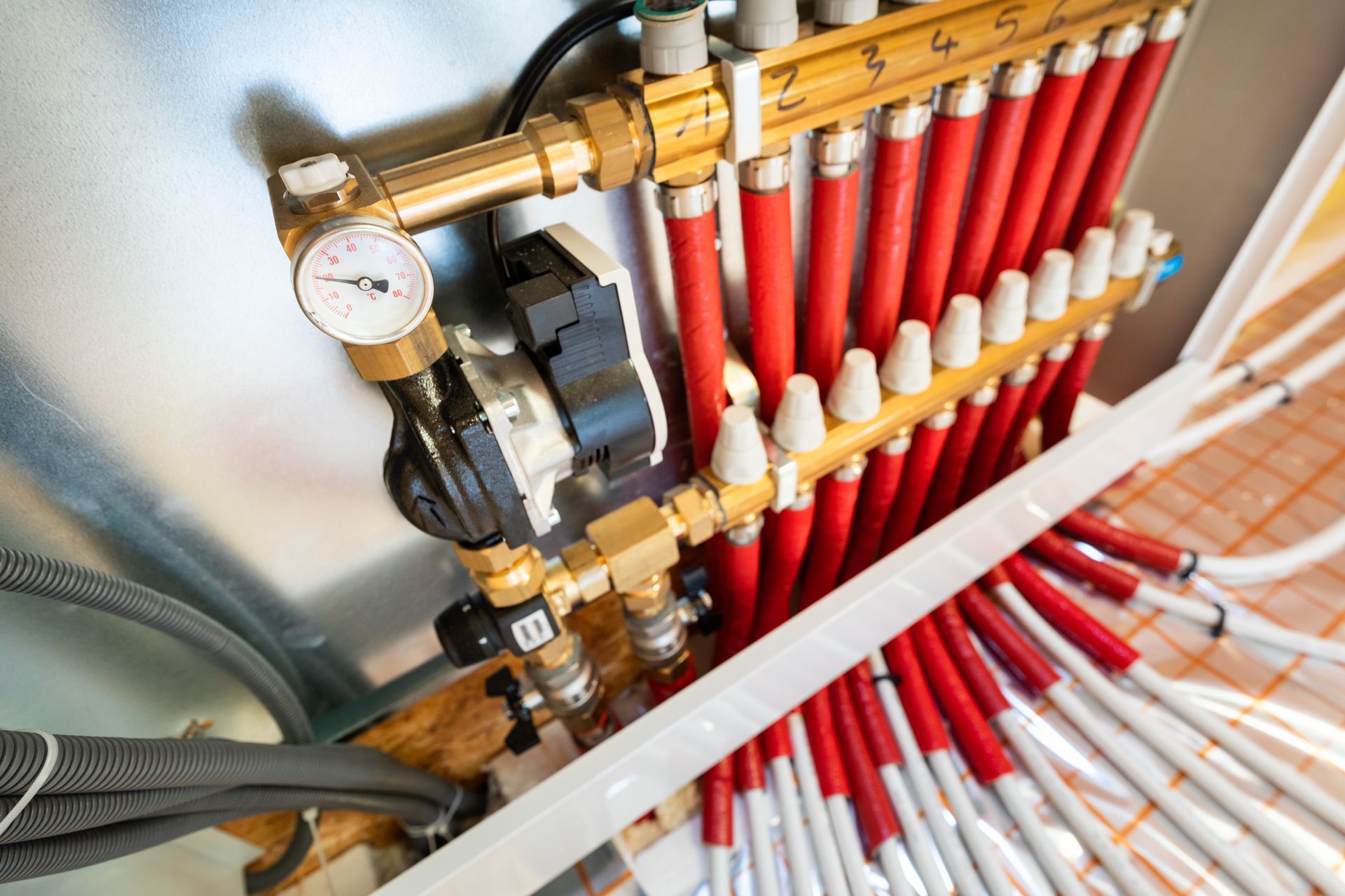 Close-up of brass plumbing manifold with red pipes and pressure gauge in a utility room Close-up of brass plumbing manifold with red pipes and pressure gauge in a utility room