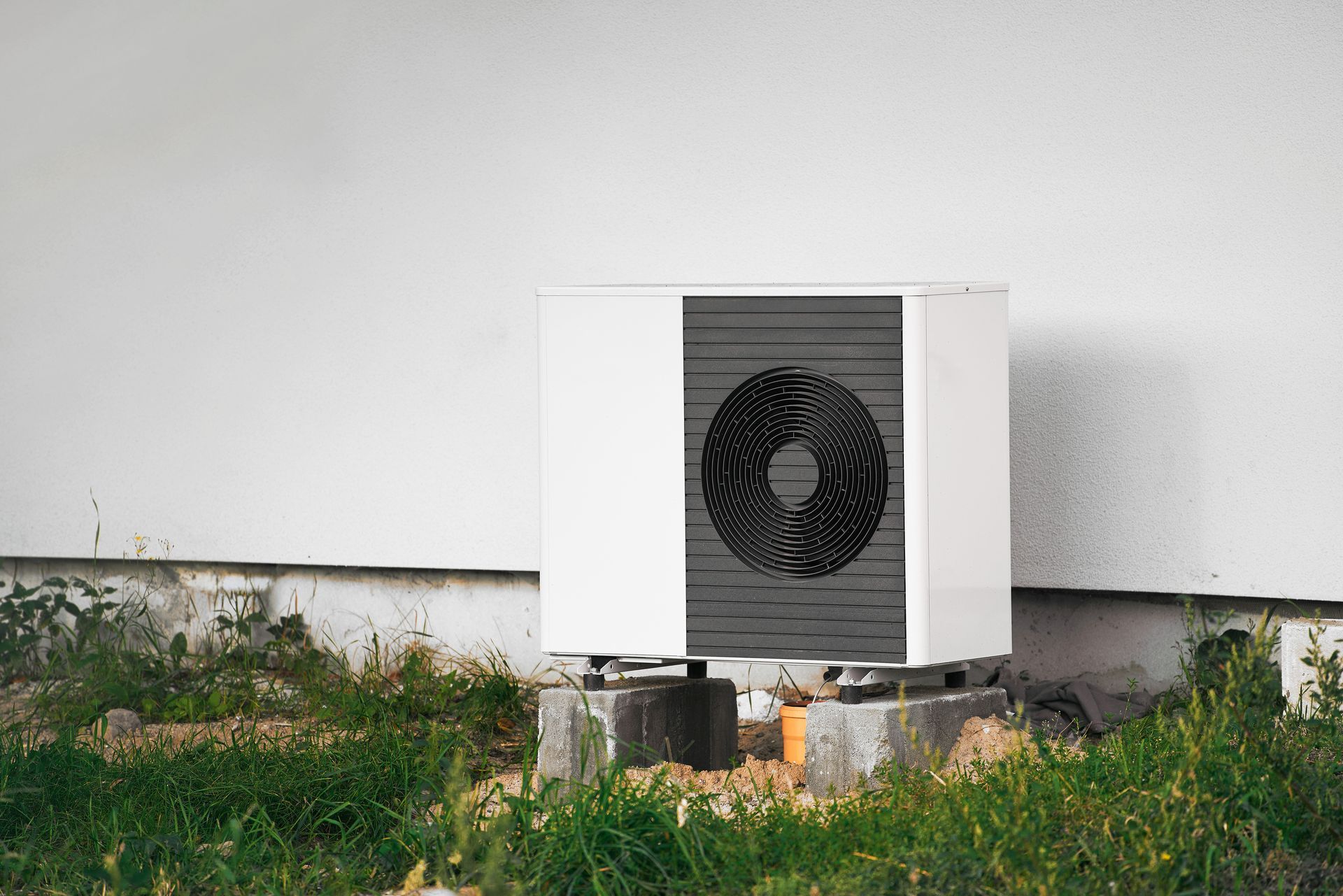 Outdoor air conditioner unit beside a white house wall above grass with a shadowed window fan grille Outdoor air conditioner unit beside a white house wall above grass with a shadowed window fan grille