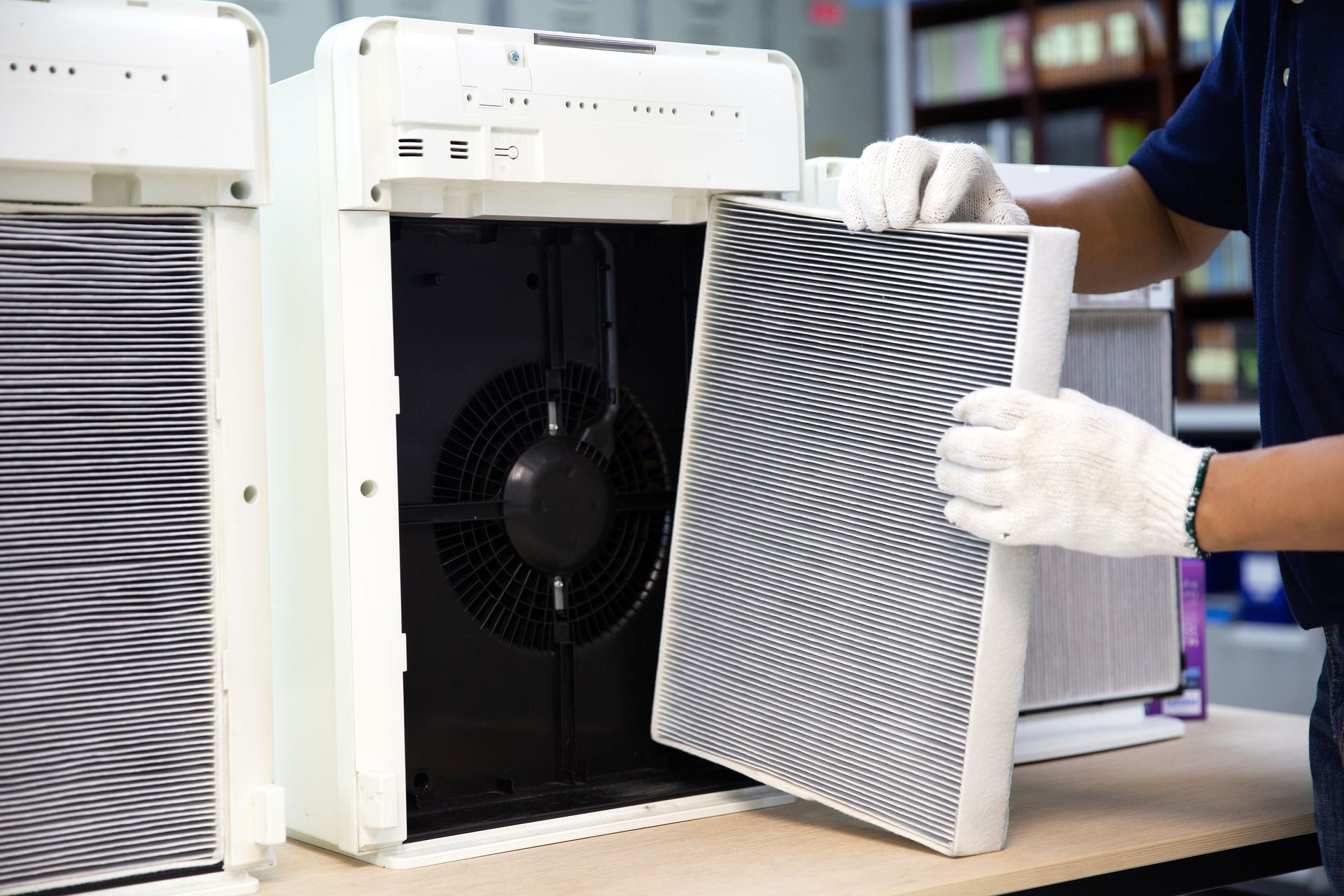 Person replacing a white air purifier filter beside a black fan unit Person replacing a white air purifier filter beside a black fan unit
