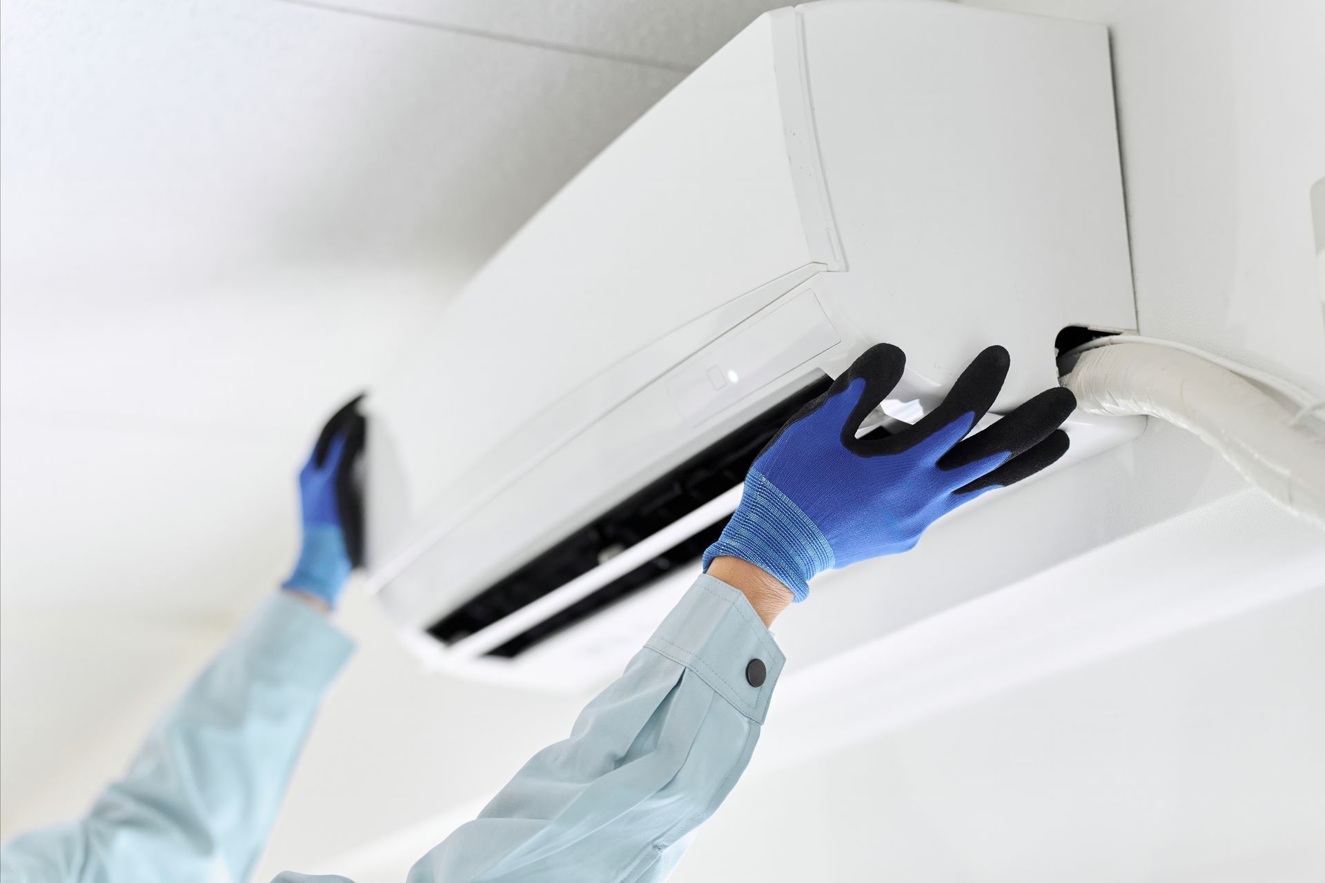 Technician cleaning a wall-mounted air conditioner with blue gloves Technician cleaning a wall-mounted air conditioner with blue gloves