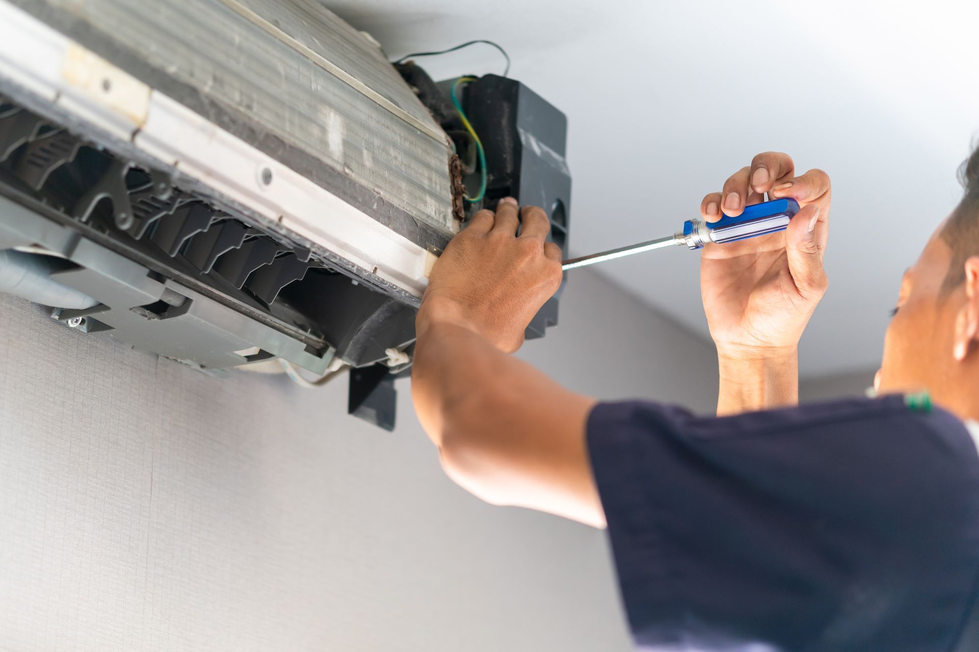 Technician using a screwdriver to repair a wall-mounted air conditioner indoors