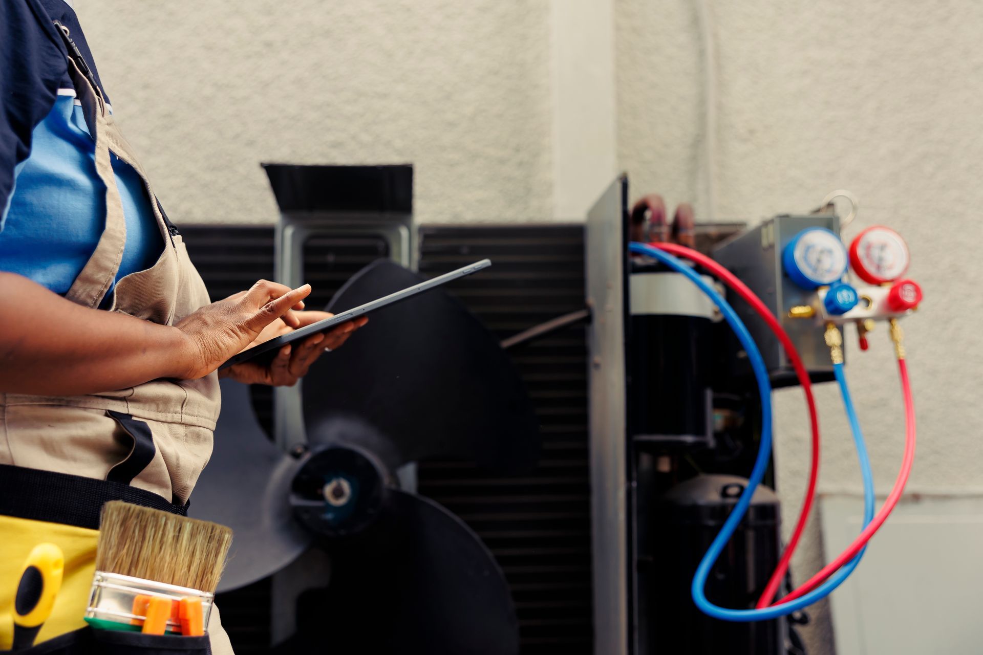 Technician holding a clipboard beside HVAC unit and pressure gauges with red and blue hoses Technician holding a clipboard beside HVAC unit and pressure gauges with red and blue hoses