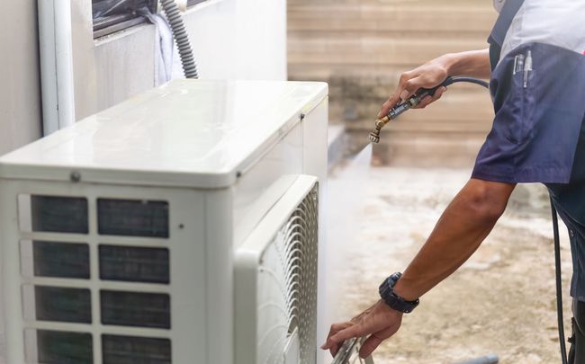 Technician spraying and cleaning an outdoor air conditioning unit beside a building stairs. Technician spraying and cleaning an outdoor air conditioning unit beside a building stairs.